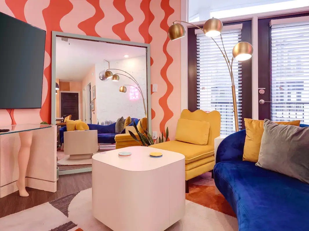 Orange und rosa verschnörkelte Wände.  Ein gelber Senfstuhl und eine blaue Samtcouch.
