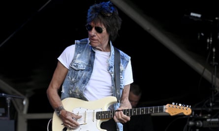 Beck spielt Gitarre auf der Bühne, in weißem T-Shirt und ärmelloser Jeansjacke.