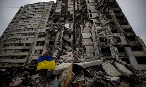 Eine Frau mit ukrainischer Flagge inspiziert ein zerstörtes Wohnhaus in Charkiw.