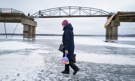 Eine Frau geht über den zugefrorenen Fluss Siverskyi Donets, während Arbeiter eine bombardierte Brücke in Staryi Saltiv reparieren.