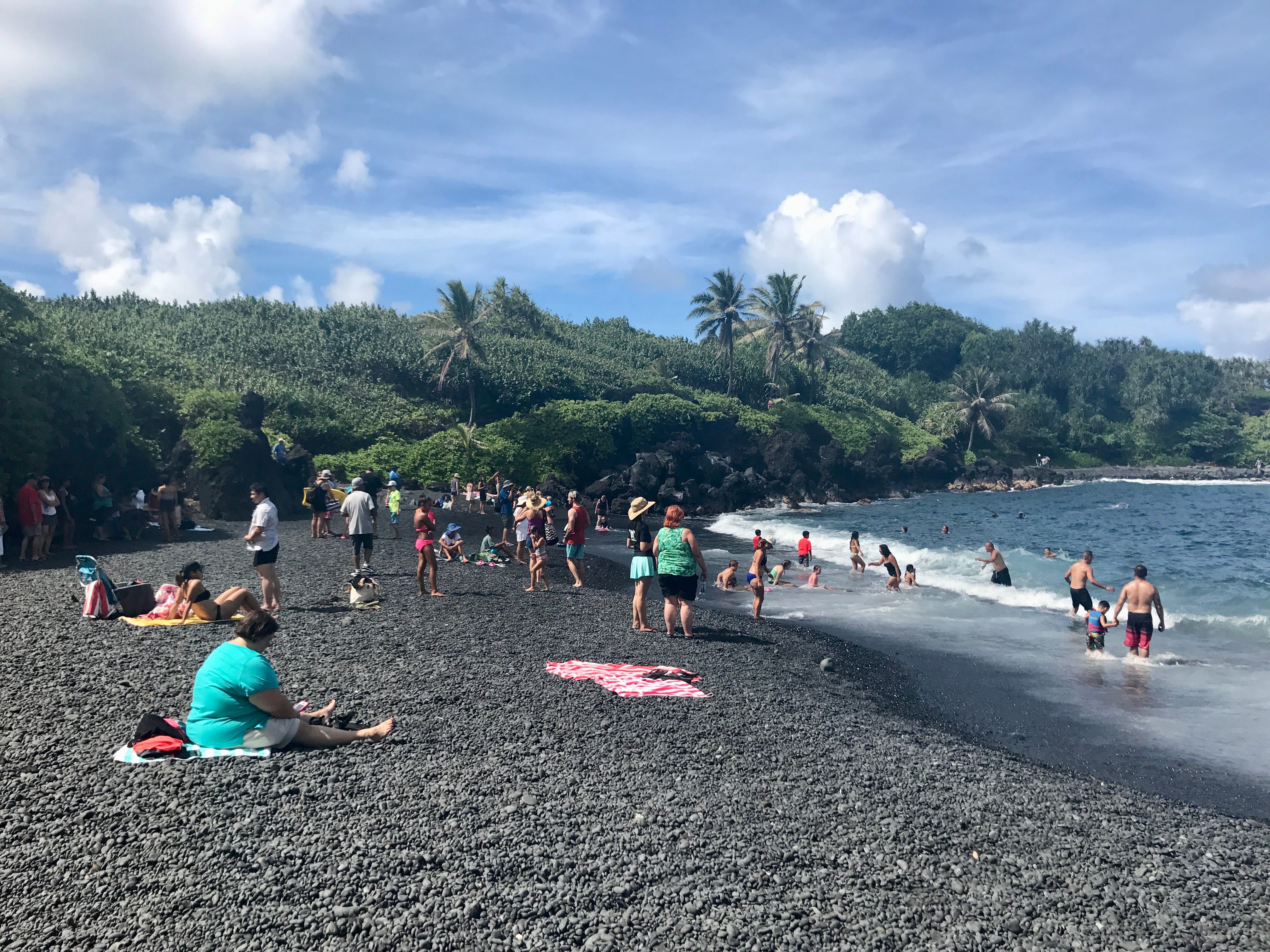 Menschen am schwarzen Sandstrand im Waiʻānapanapa State Park.  Maui, Hawaii