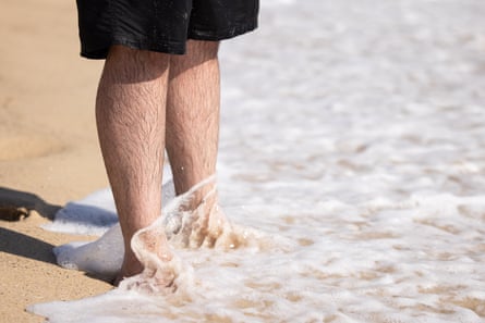 Mostafa Rachwani steht am Strand, Wasser rauscht über seine Füße