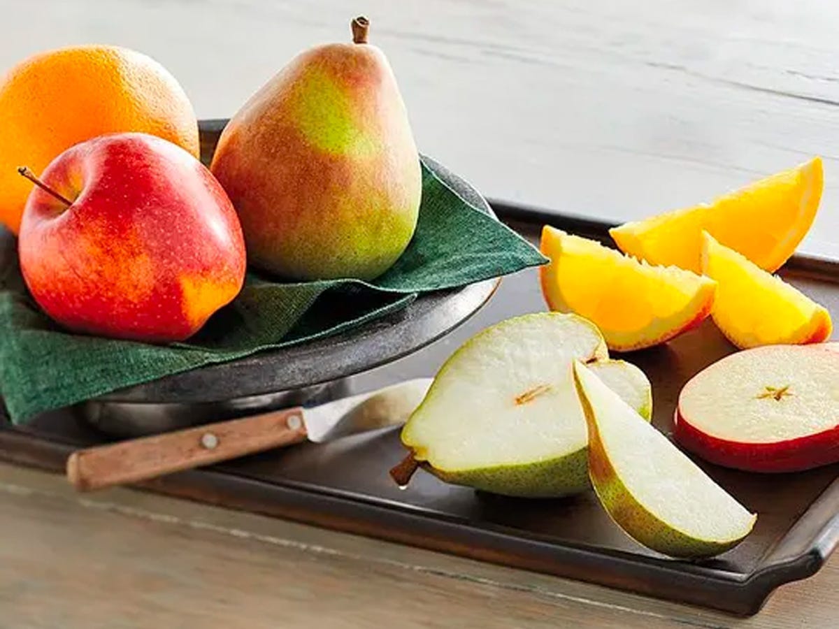 Ganze und geschnittene Birnen, Äpfel, Orangen, die zusammen mit einem Schälmesser auf einem Tablett angeordnet sind