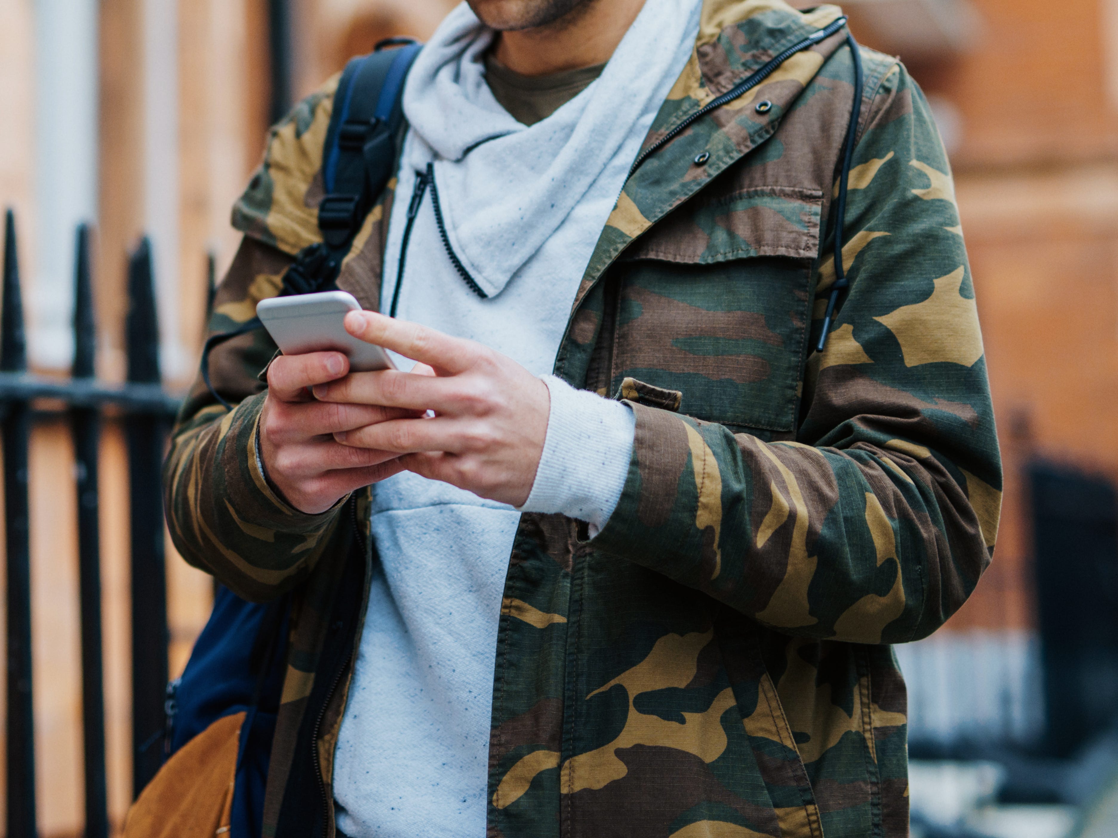 Mann, der eine Jacke mit Tarnmuster trägt, während er SMS schreibt und eine Straße entlang geht