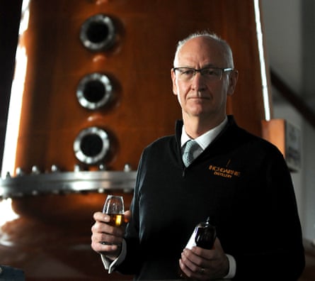 Ian Palmer vor einer glänzenden Kupferdestille mit einem Glas Whiskey in der Hand