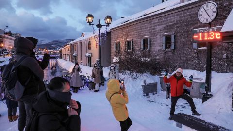 Touristen posieren für Fotos vor einem Thermometer, das -11,3 Grad Celsius (11,6 F) anzeigt, in Otaru, Präfektur Hokkaido im Norden Japans am 24. Januar 2023.