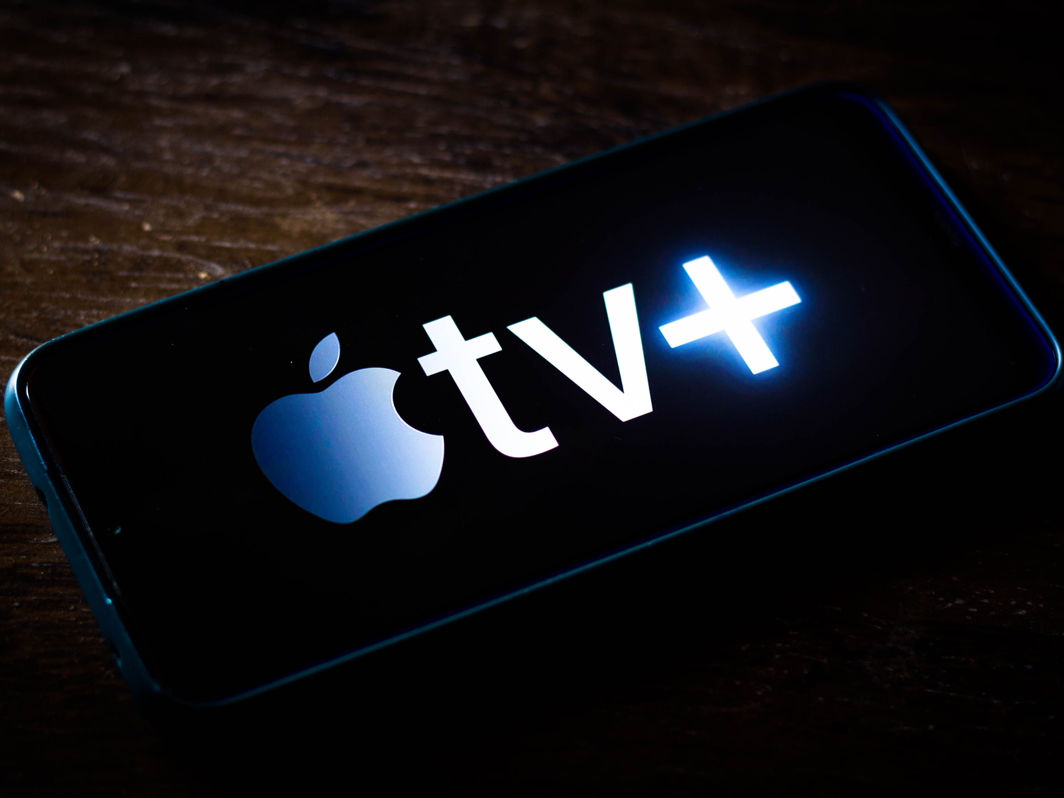 apple tv plus logo auf einem smartphone auf einer dunklen holzoberfläche