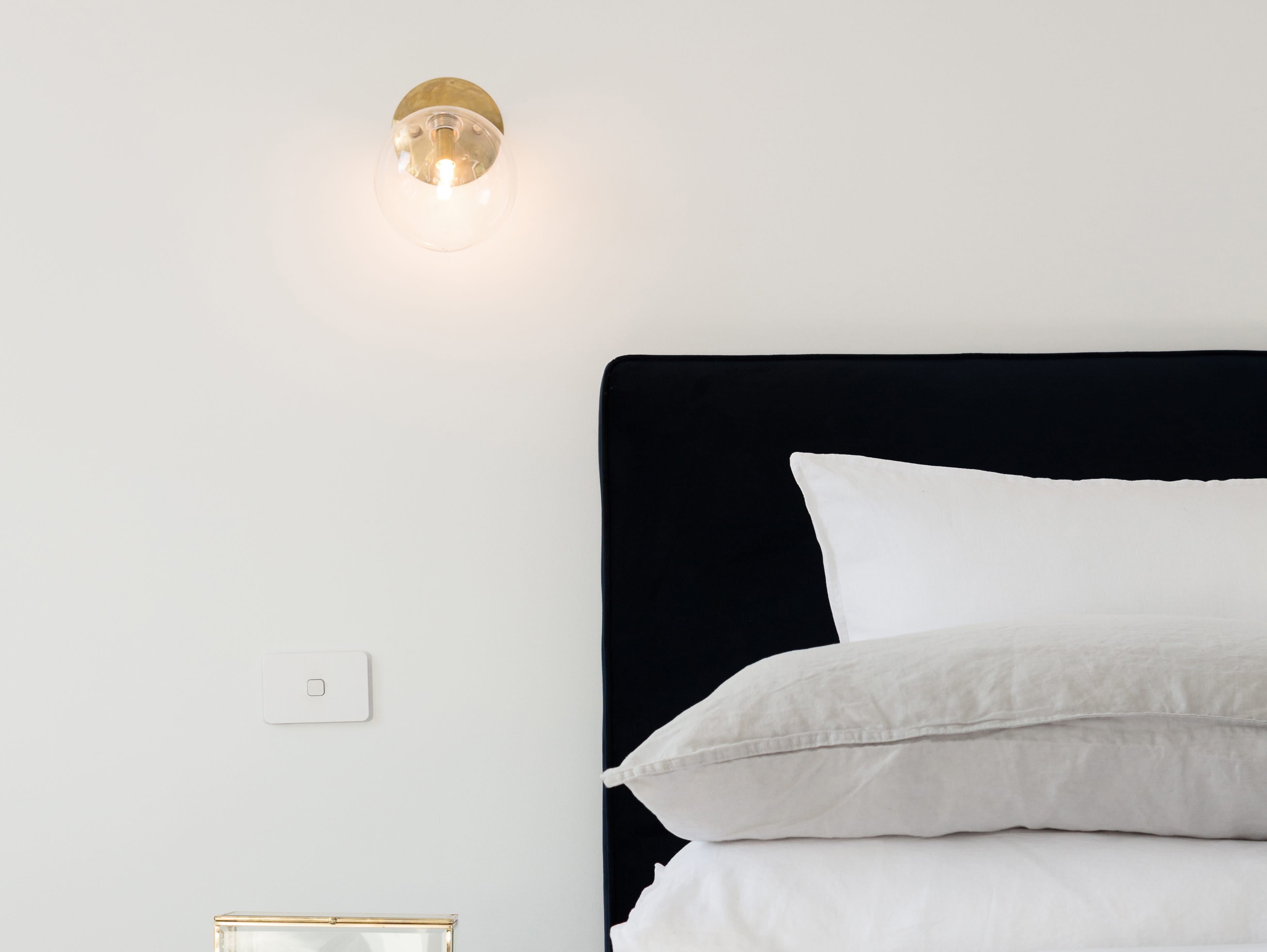 Ein Bett mit grauen und weißen Laken, daneben eine beleuchtete Wandlampe