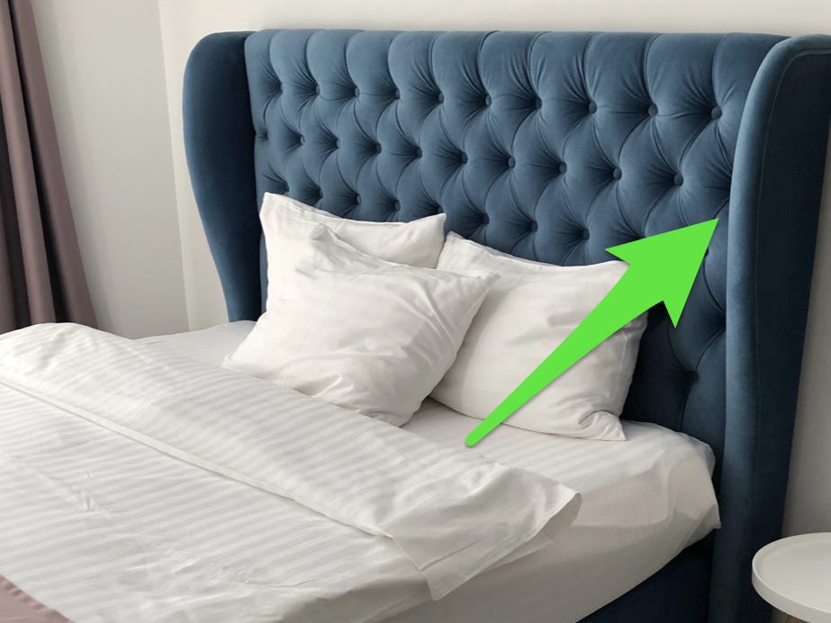 Ein Bett mit weißen Laken und einem blauen, geschwungenen Kopfteil mit einem grünen Pfeil, der auf das Kopfteil zeigt