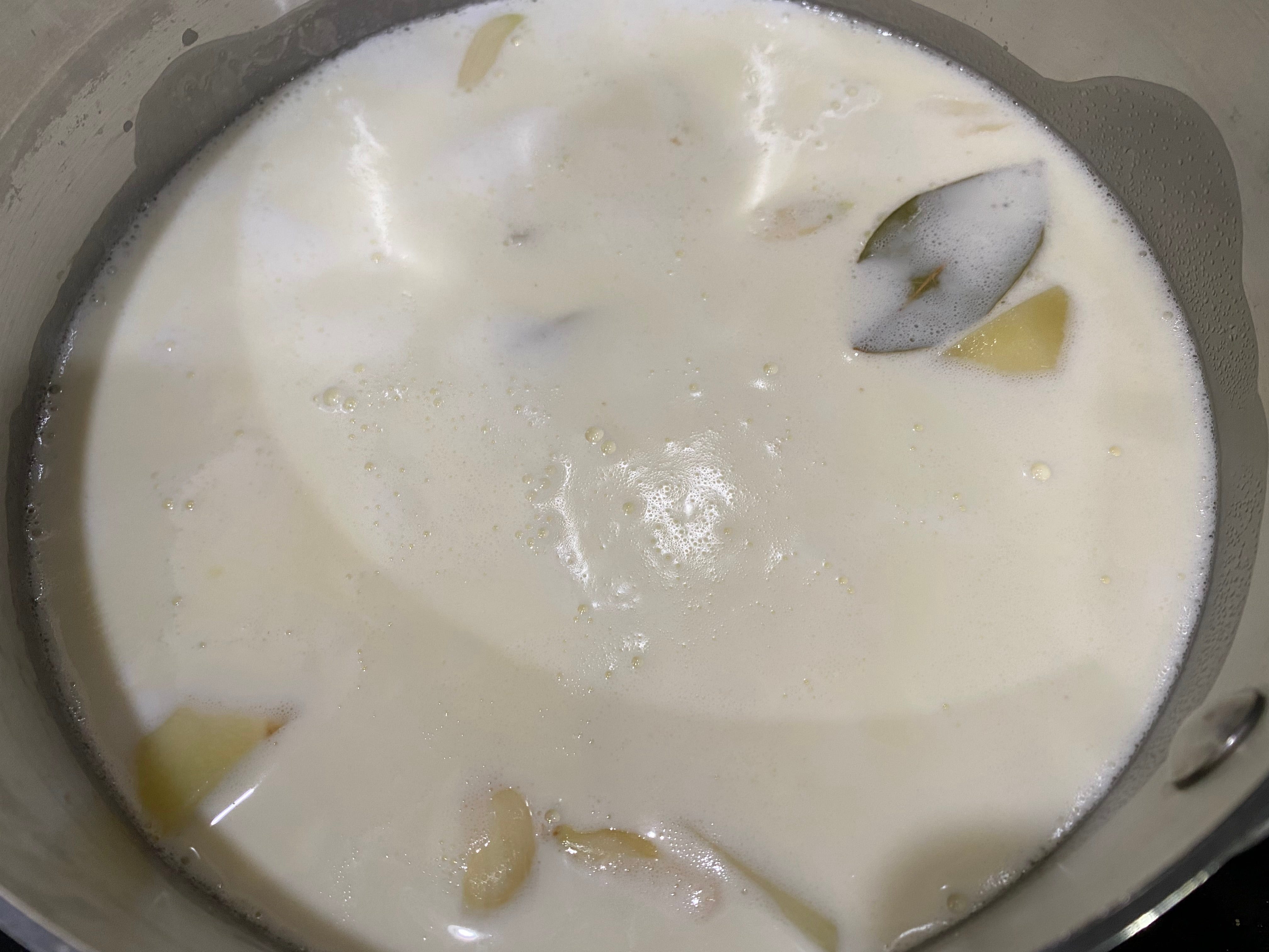 Yukon Gold-Kartoffeln, zwei zerdrückte Knoblauchzehen und ein Lorbeerblatt im Topf voller Milchprodukte