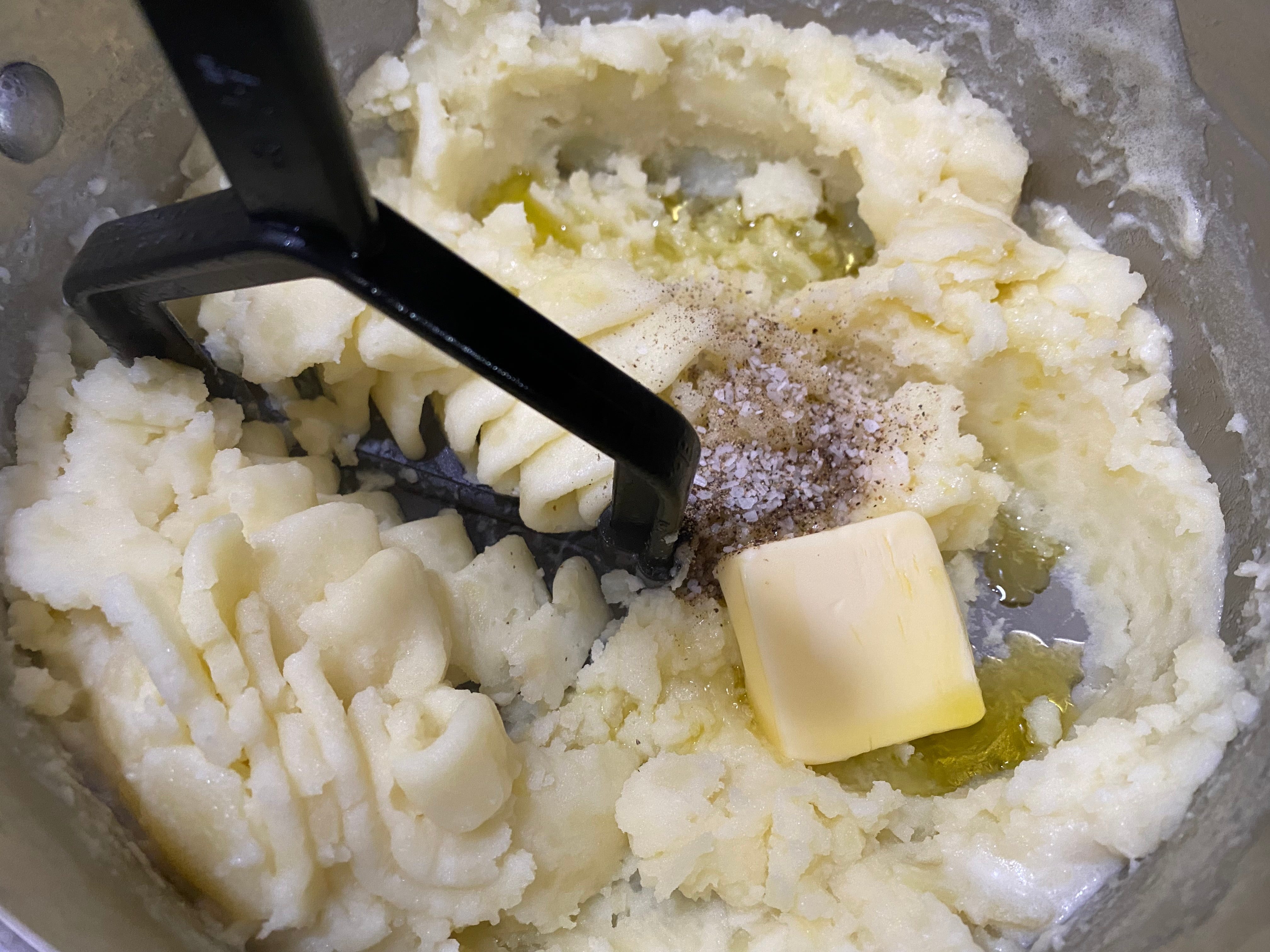 Die Kartoffeln werden in der Schüssel zerdrückt, während Gewürze, Olivenöl und Butter untergemischt werden.