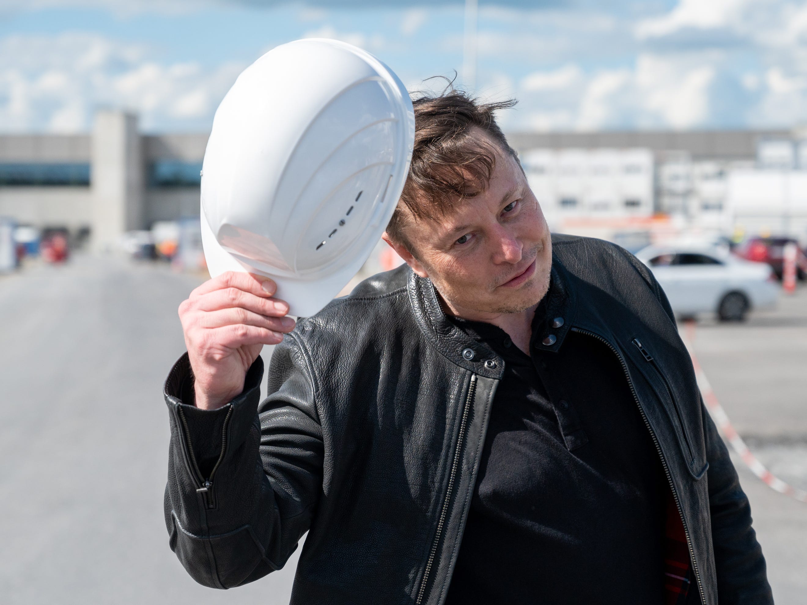 Elon Mush hält einen Schutzhelm mit Tesla-Logo.