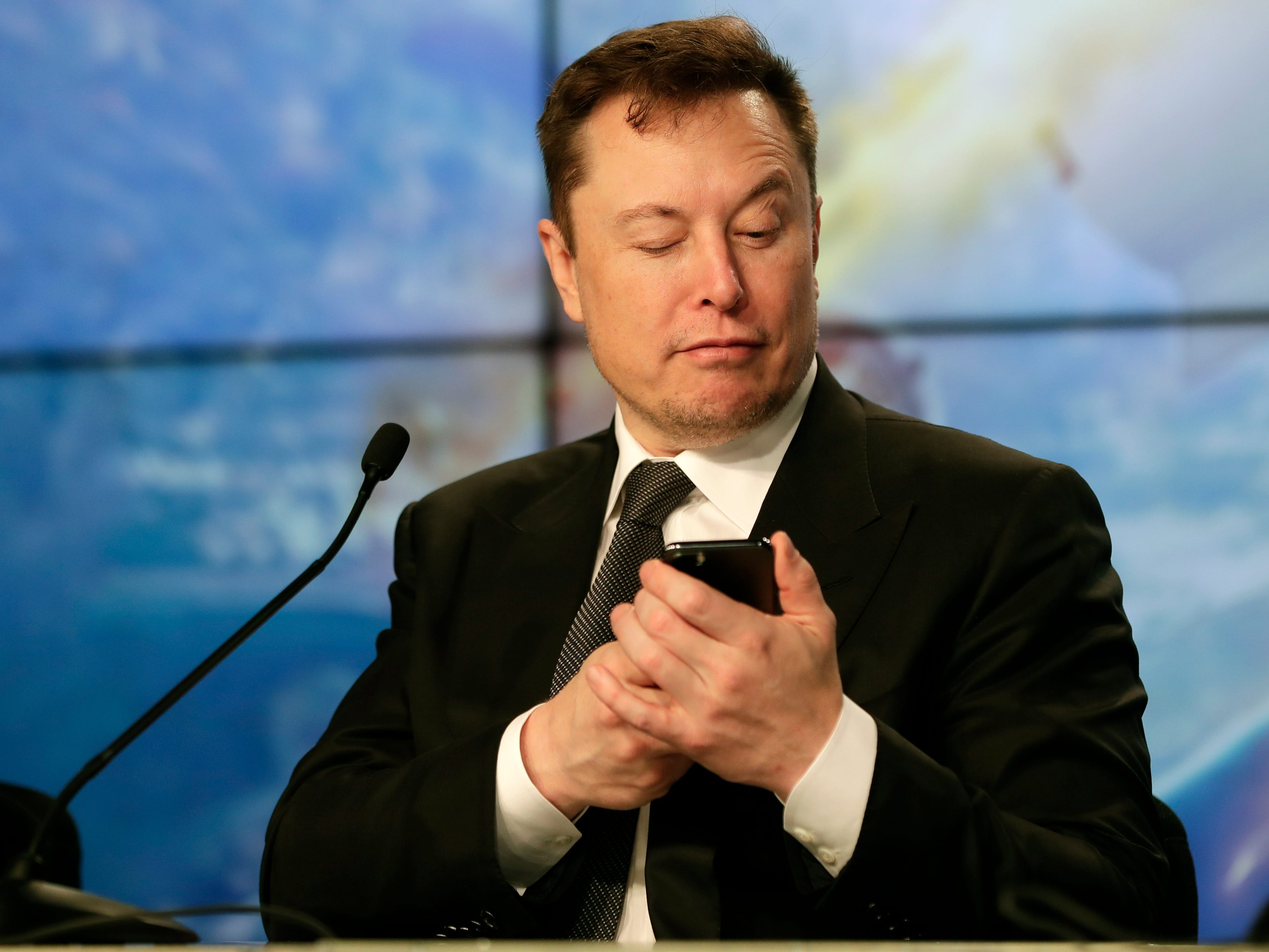 Elon Musk schaut auf sein Handy.