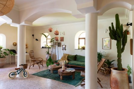 Ein Wohnbereich mit Bogenfenstern, die Licht hereinlassen, und Bögen und Säulen im Inneren, einer Lounge und Stühlen, einem Kinderfahrrad und einem Indoor-Kaktus