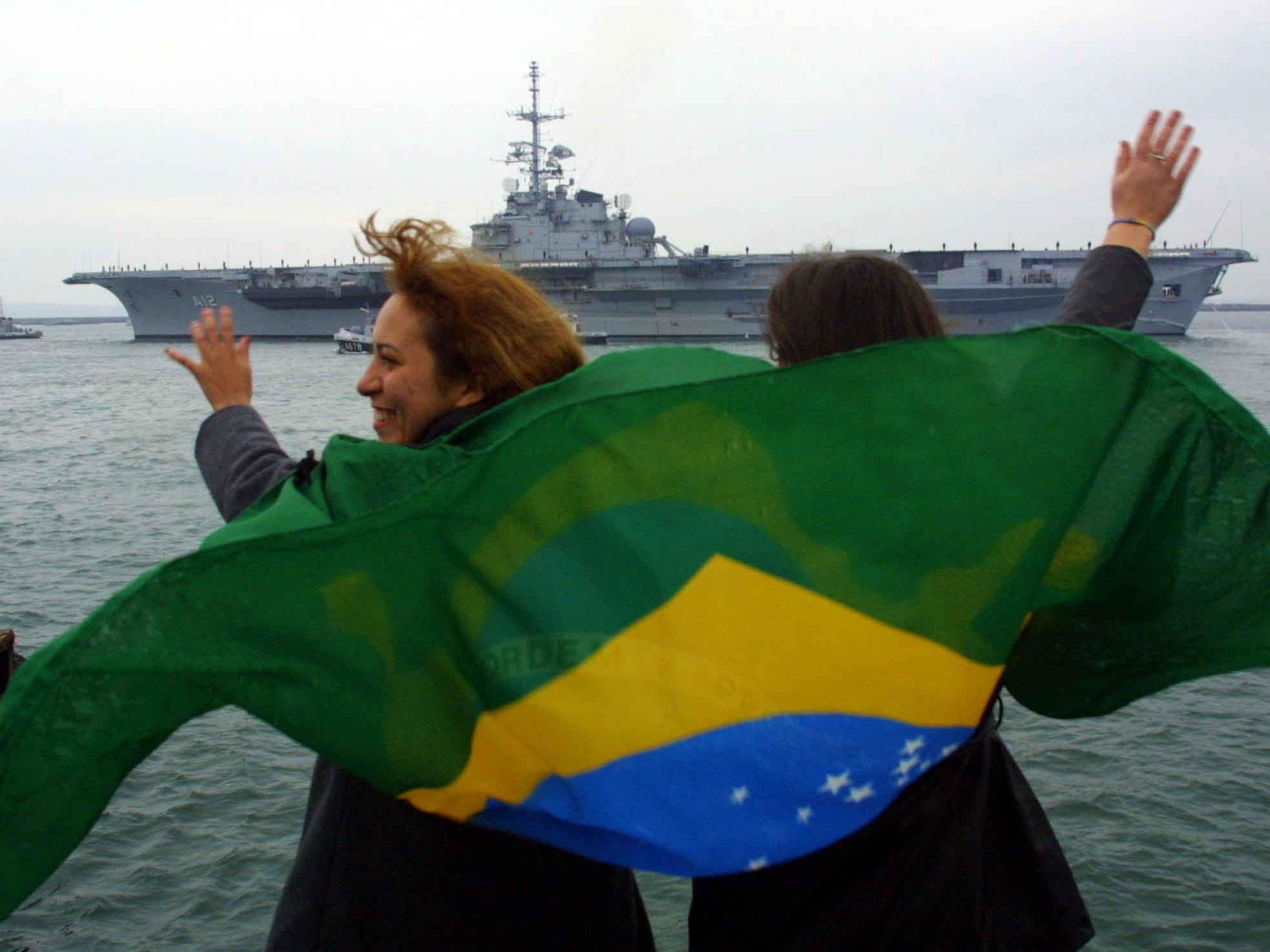 Zwei brasilianische Frauen schwenken eine Nationalflagge, als der ehemalige französische Flugzeugträger 