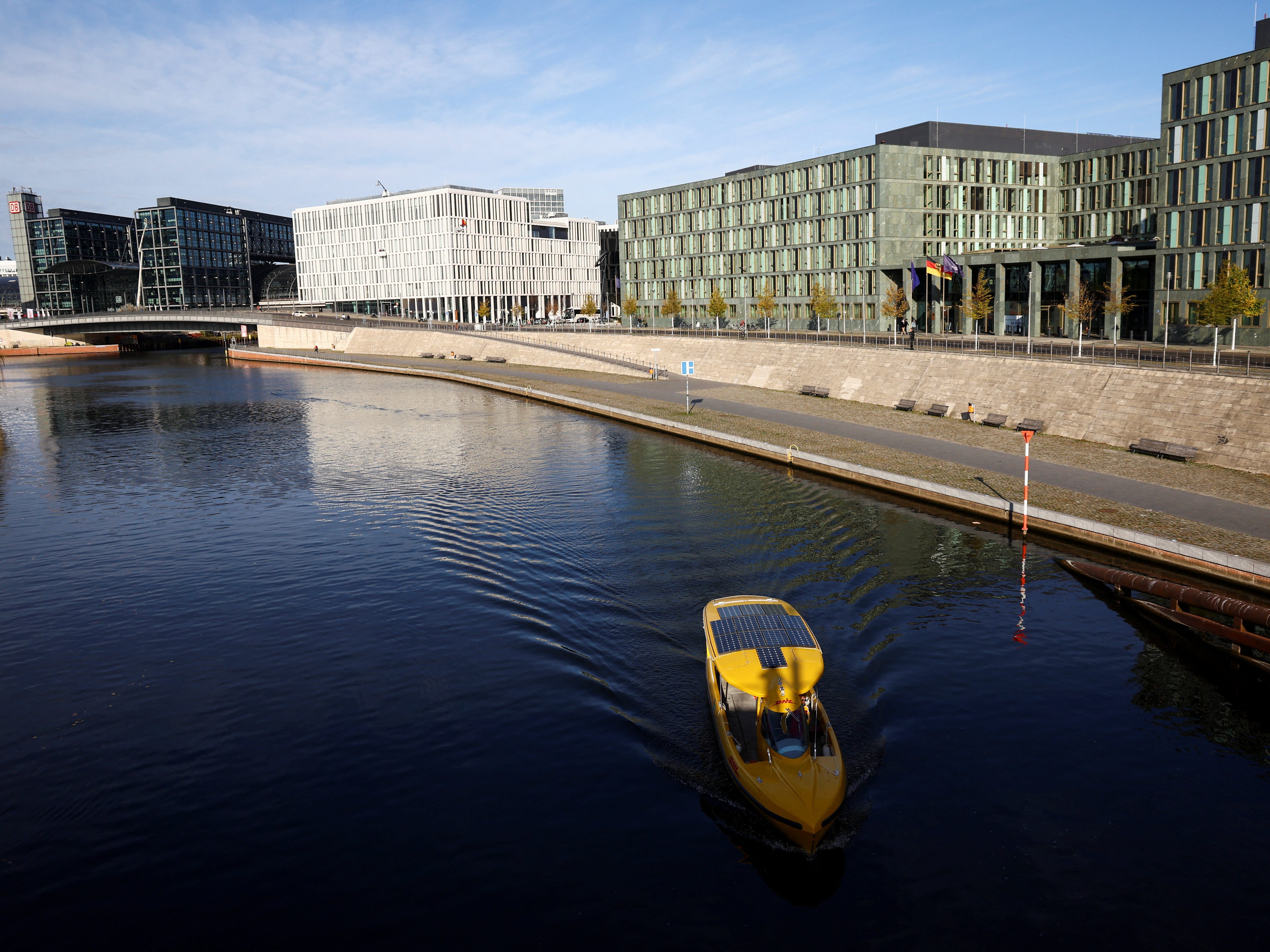Ein leuchtend gelbes Boot fährt einen sehr ruhigen Fluss vor Bürogebäuden in Berlin hinunter.