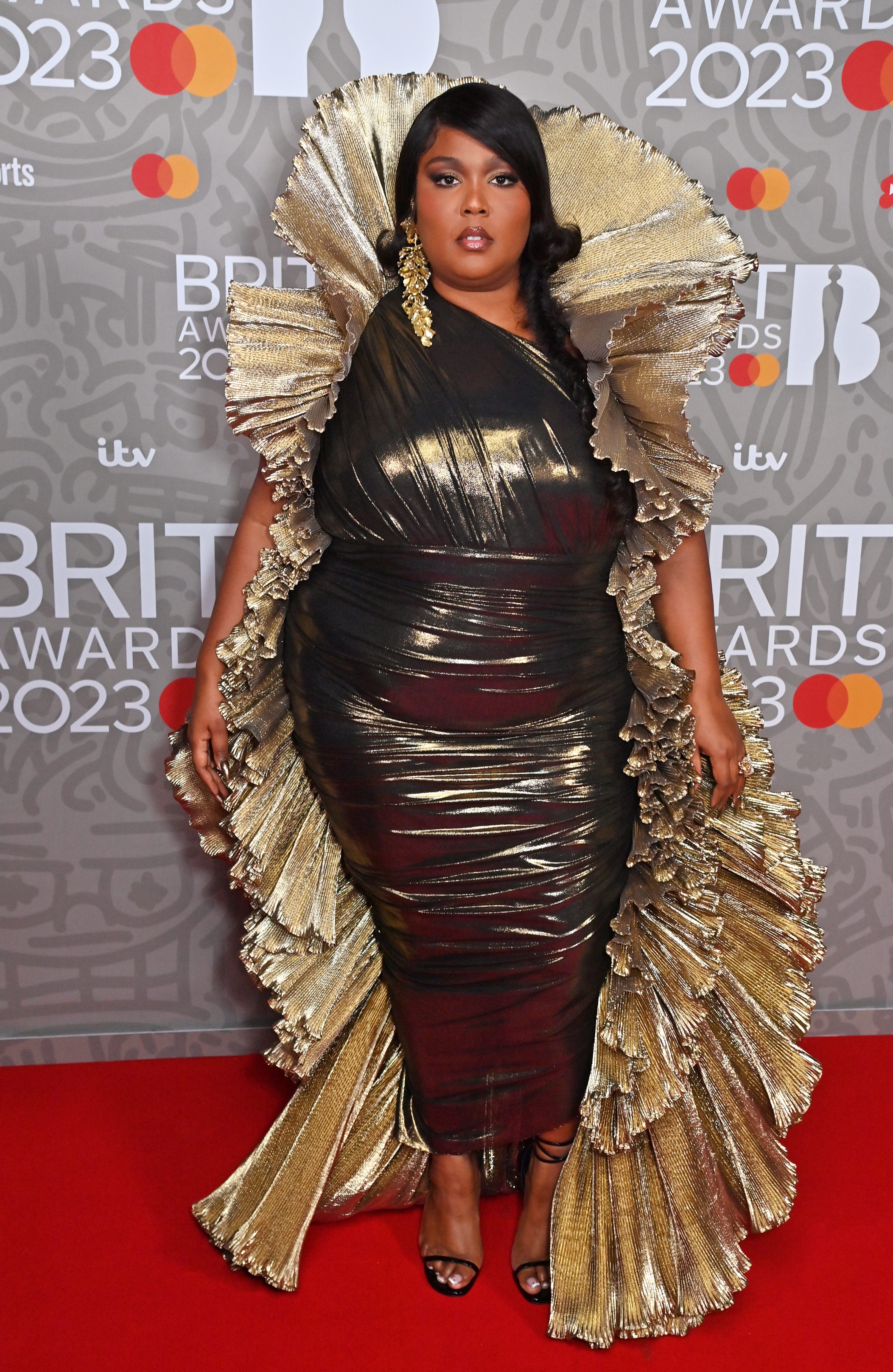 Lizzo in einem metallischen Kleid und einem goldenen Umhang auf dem roten Teppich der Brit Awards 2023