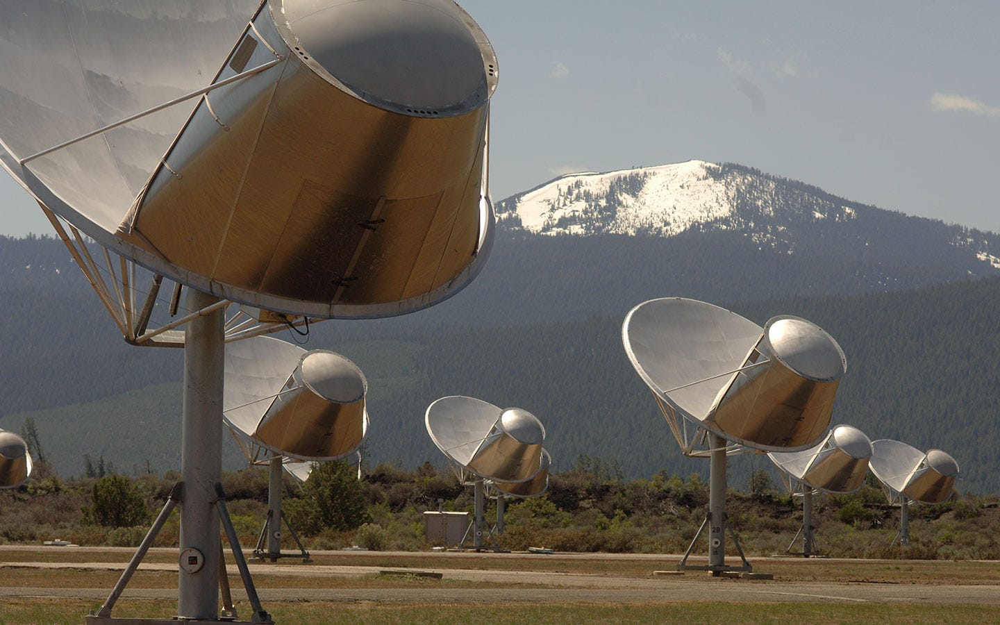 Radioteleskopschüsseln zeigten in einem offenen Feld mit schneebedeckten Bergen im Hintergrund auf den Himmel