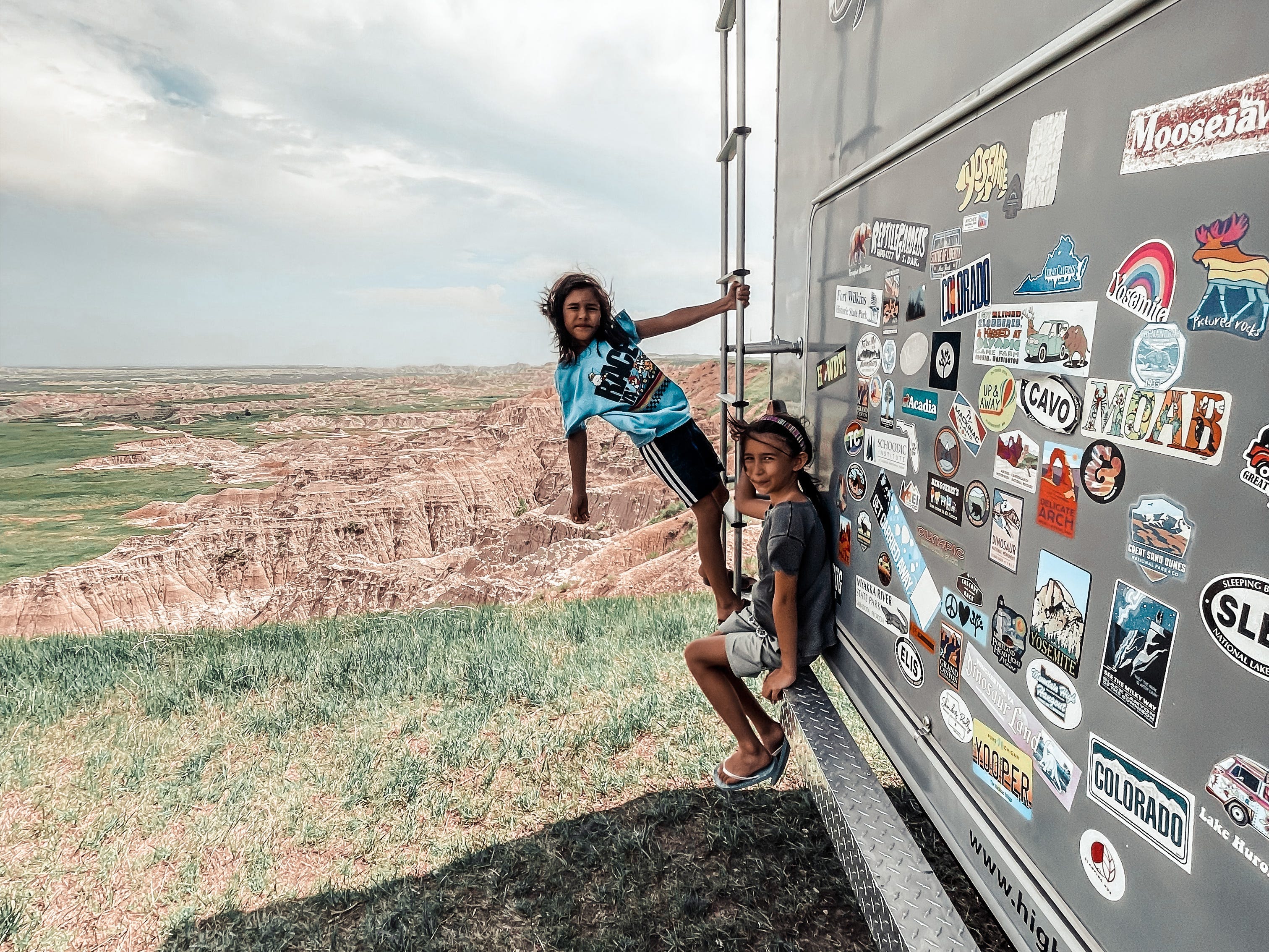 Kinder posieren auf der Seite eines großen grauen Wohnwagens mit Autoaufklebern