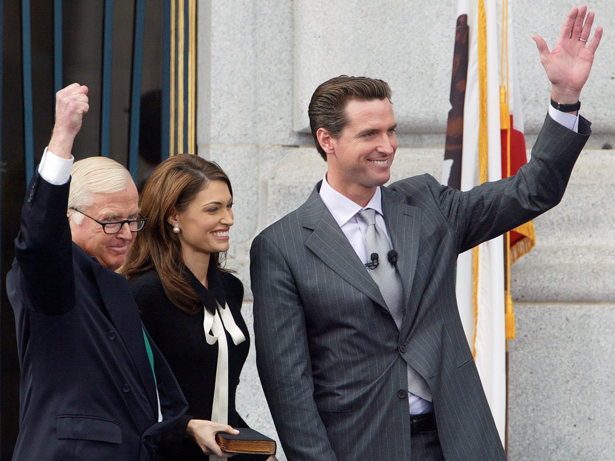 er neue Bürgermeister von San Francisco, Gavin Newsom, winkt gemeinsam mit seinem Vater Richter William Newsom und seiner Frau Kimberly Guilfoyle Newsom der Menge zu, nachdem sie den Amtseid abgelegt haben.