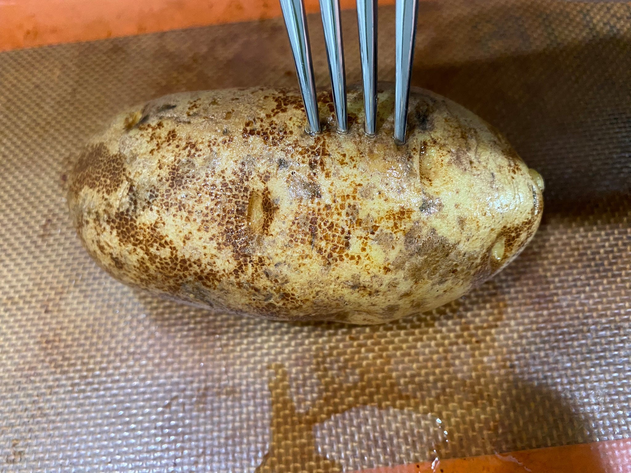 Kartoffel, die mit einer Gabel auf einem Backblech erstochen wird