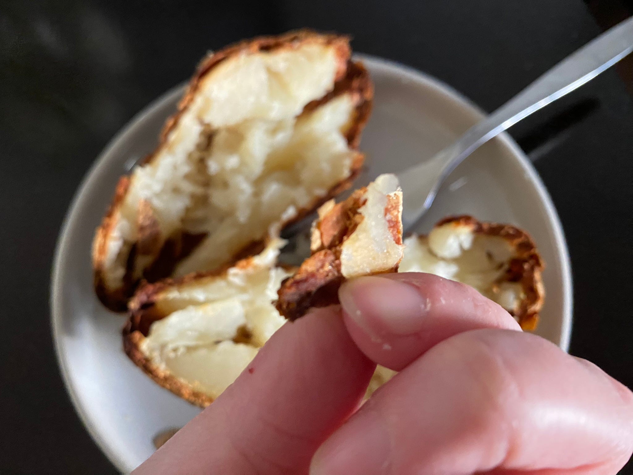 Hand, die knusprig gebackene Kartoffelhaut über einer Ofenkartoffel auf einem Teller hält