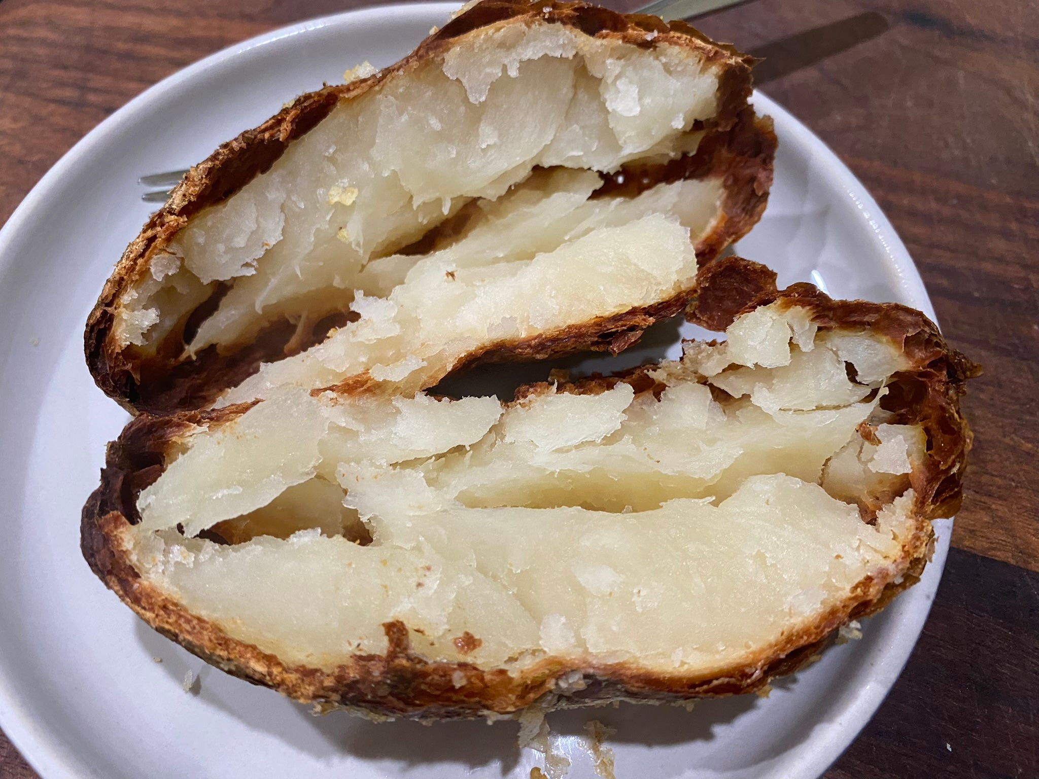 knusprig gebackene Kartoffel aufgeschnitten auf einem weißen Teller