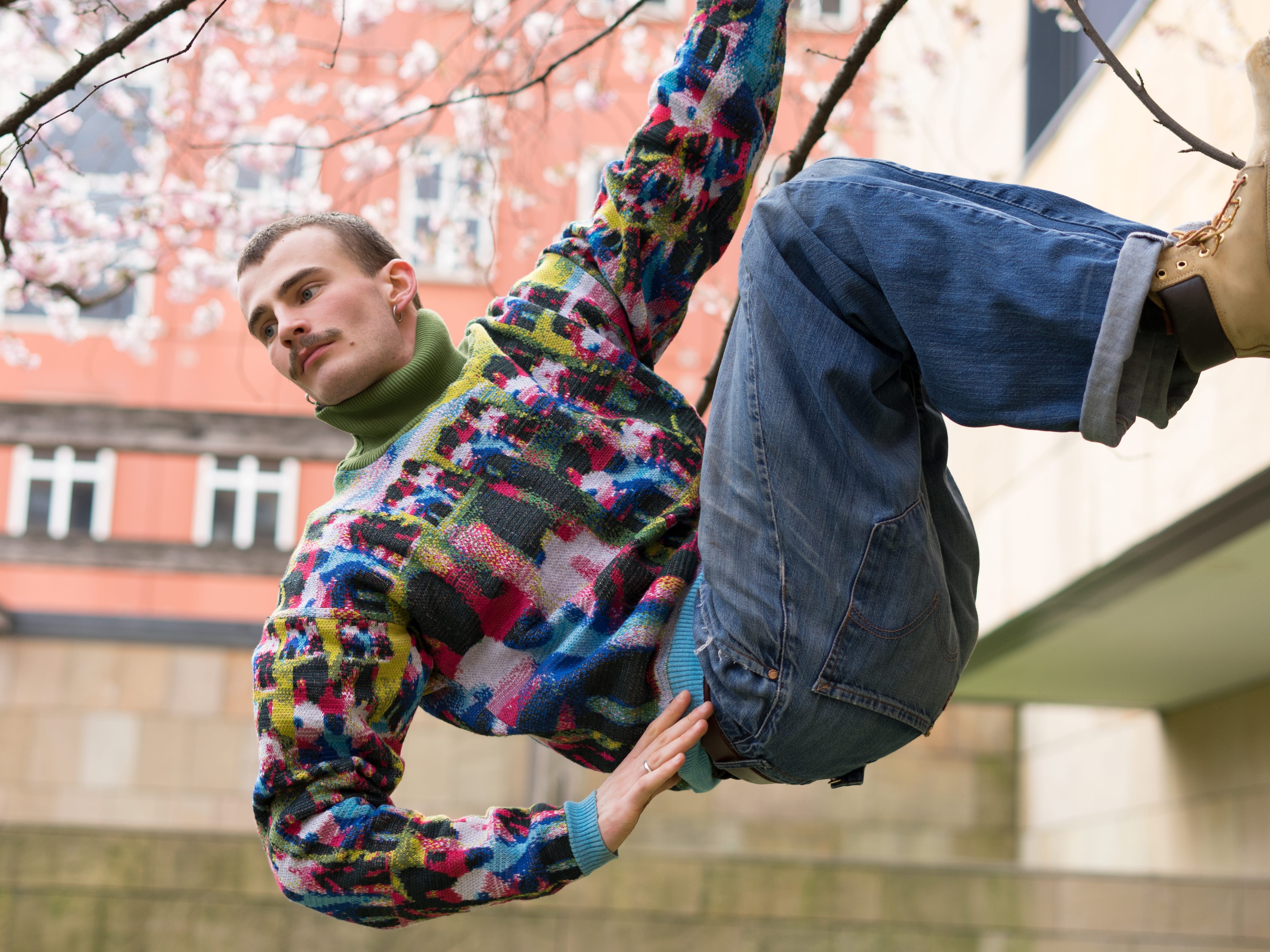 Ein Mann klettert in einem farbenfrohen Pullover und Blue Jeans eine Wand hoch