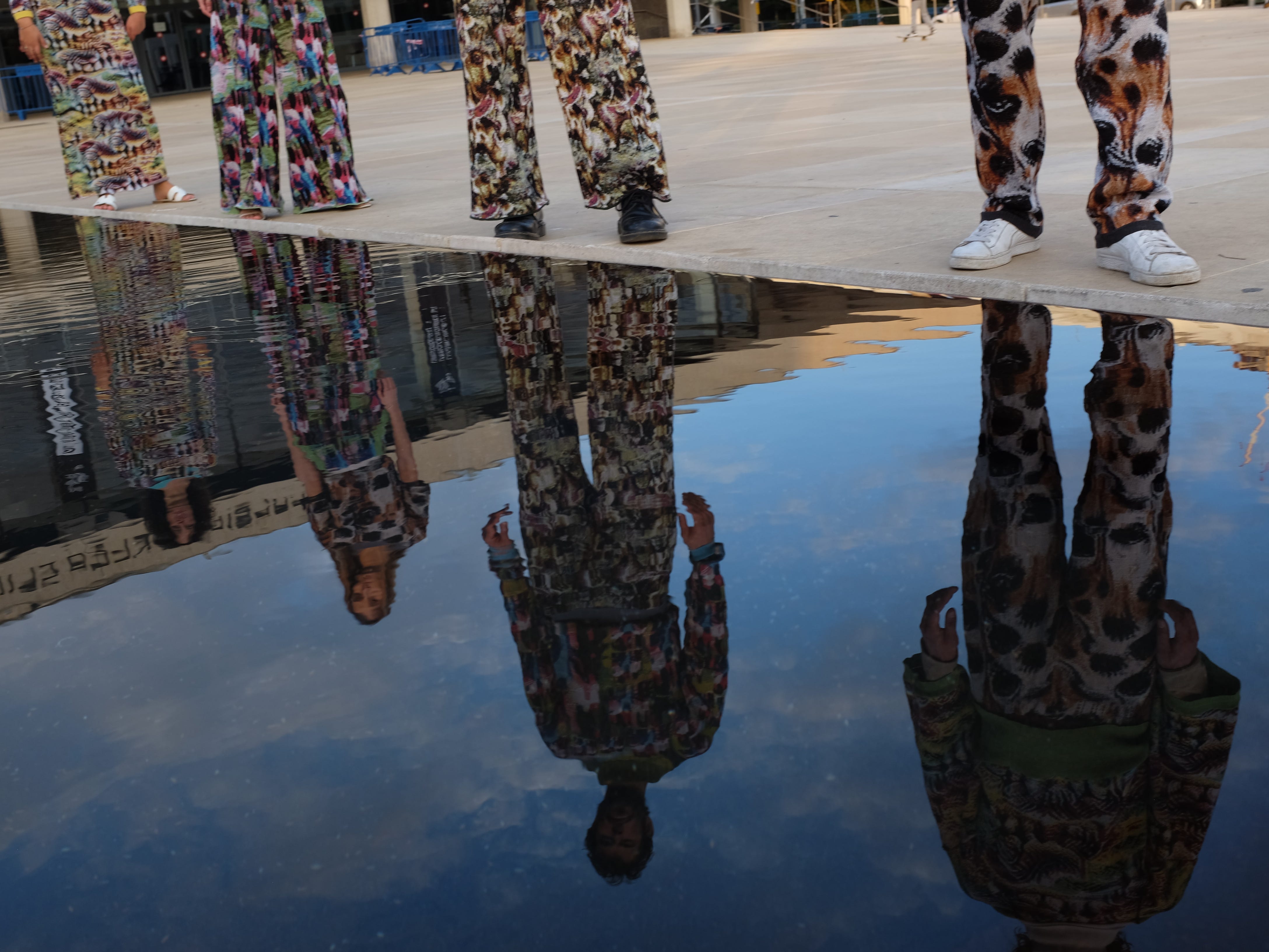 Vier Personen, die die leuchtenden Outfits von Cap_able tragen, stehen in einer Reihe und spiegeln sich im Wasser
