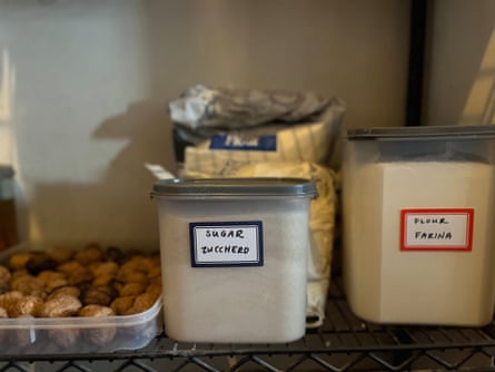 Ein Vorratsregal mit einem Tablett mit Nüssen und durchsichtigen Plastikbehältern mit Zucker und Mehl.