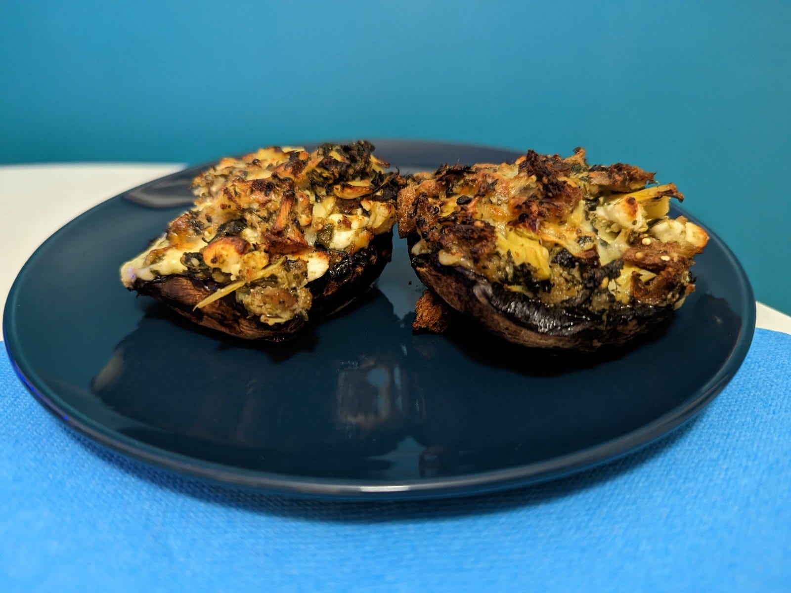 Zwei gefüllte Portobello-Pilze auf einem dunklen Teller auf einem Küchentisch