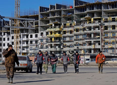 Arbeiter gehen vor einem im Bau befindlichen Wohnhaus im besetzten Mariupol.