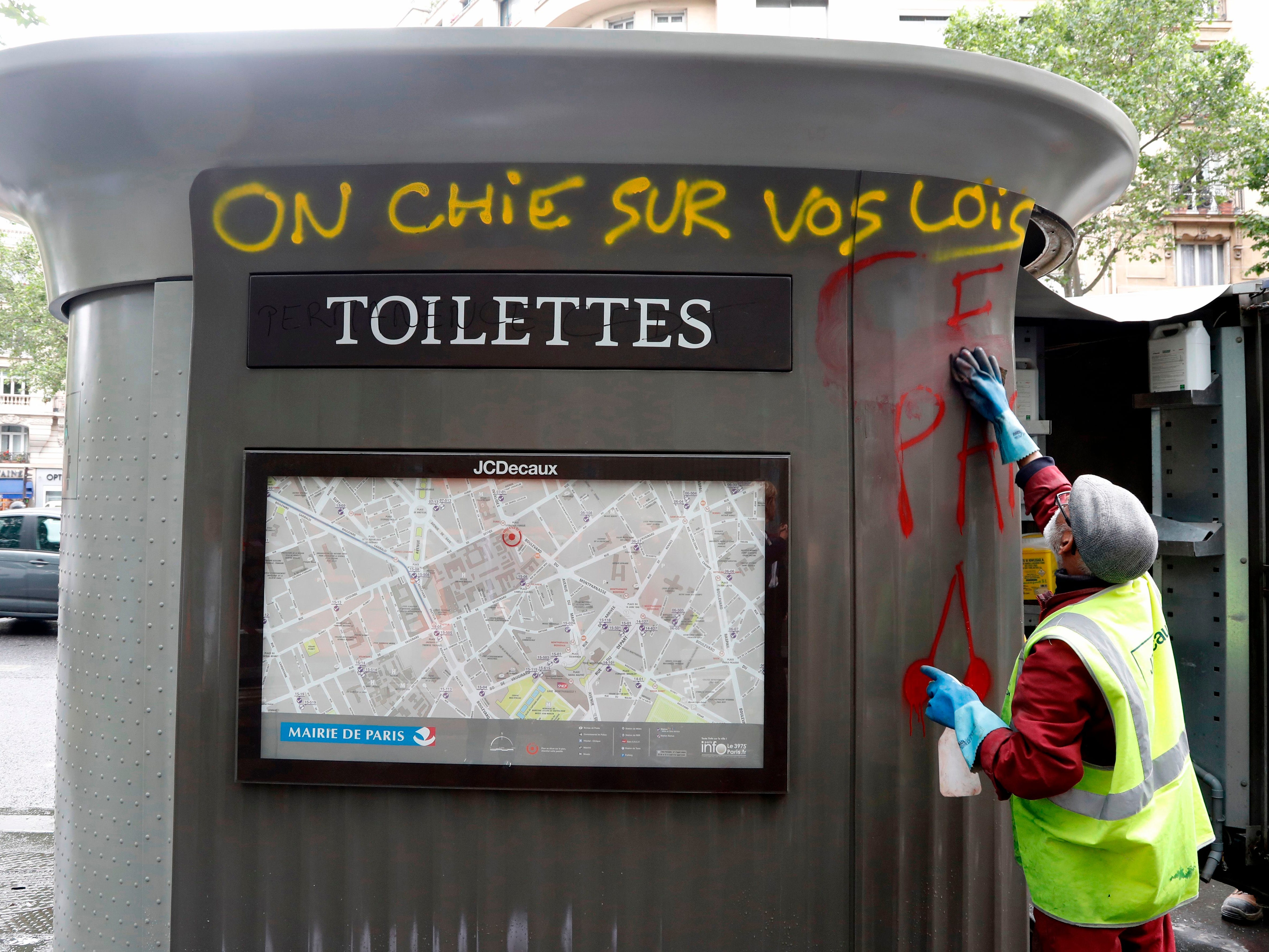 Ein Angestellter reinigt eine öffentliche Toilette, auf der auf Französisch die Worte „Wir scheißen auf Ihre Gesetze“ stehen