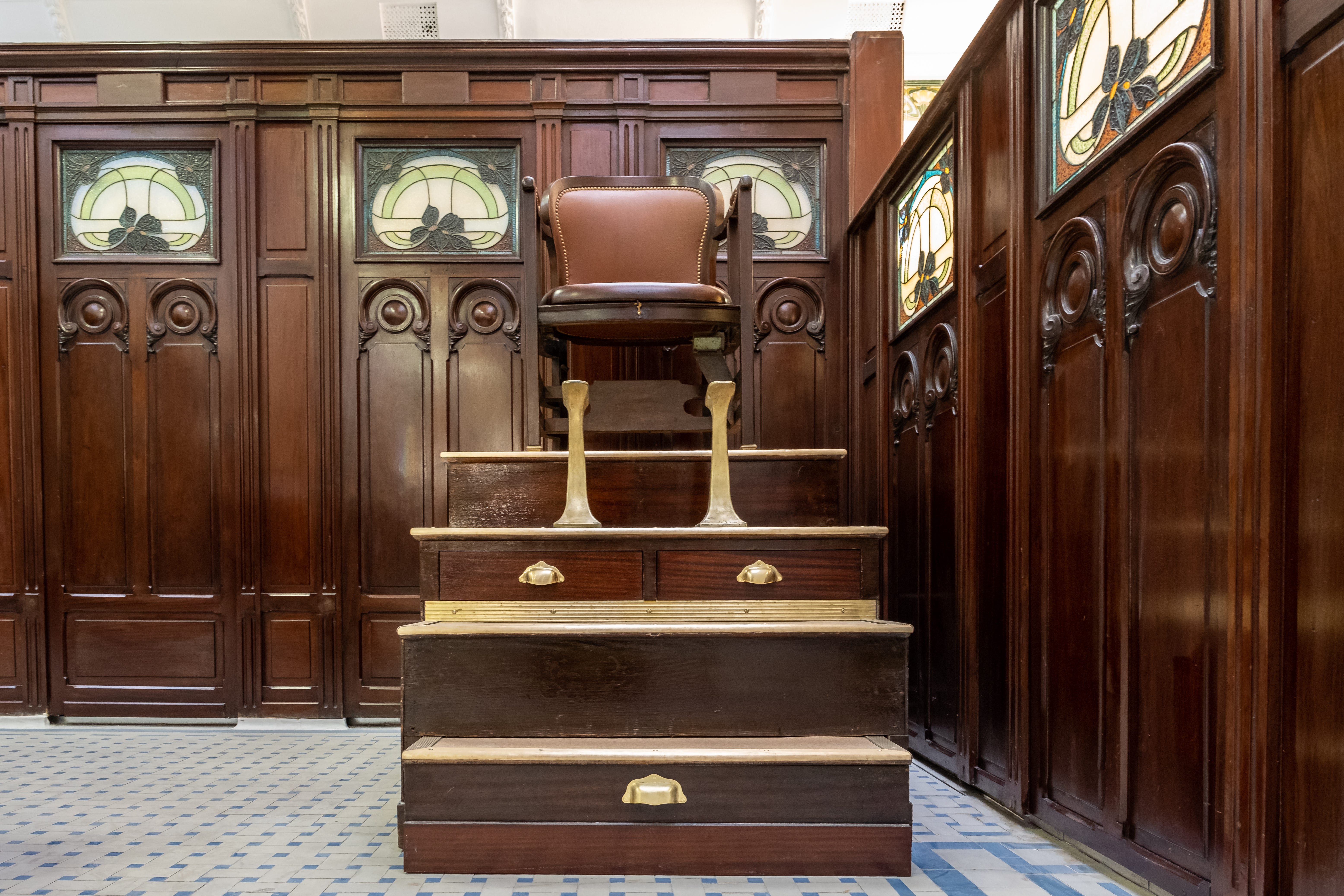 Ein alter brauner Schuhputzstuhl steht auf einer funktionalen Miniaturtreppe mit bedienbaren Schubladen.