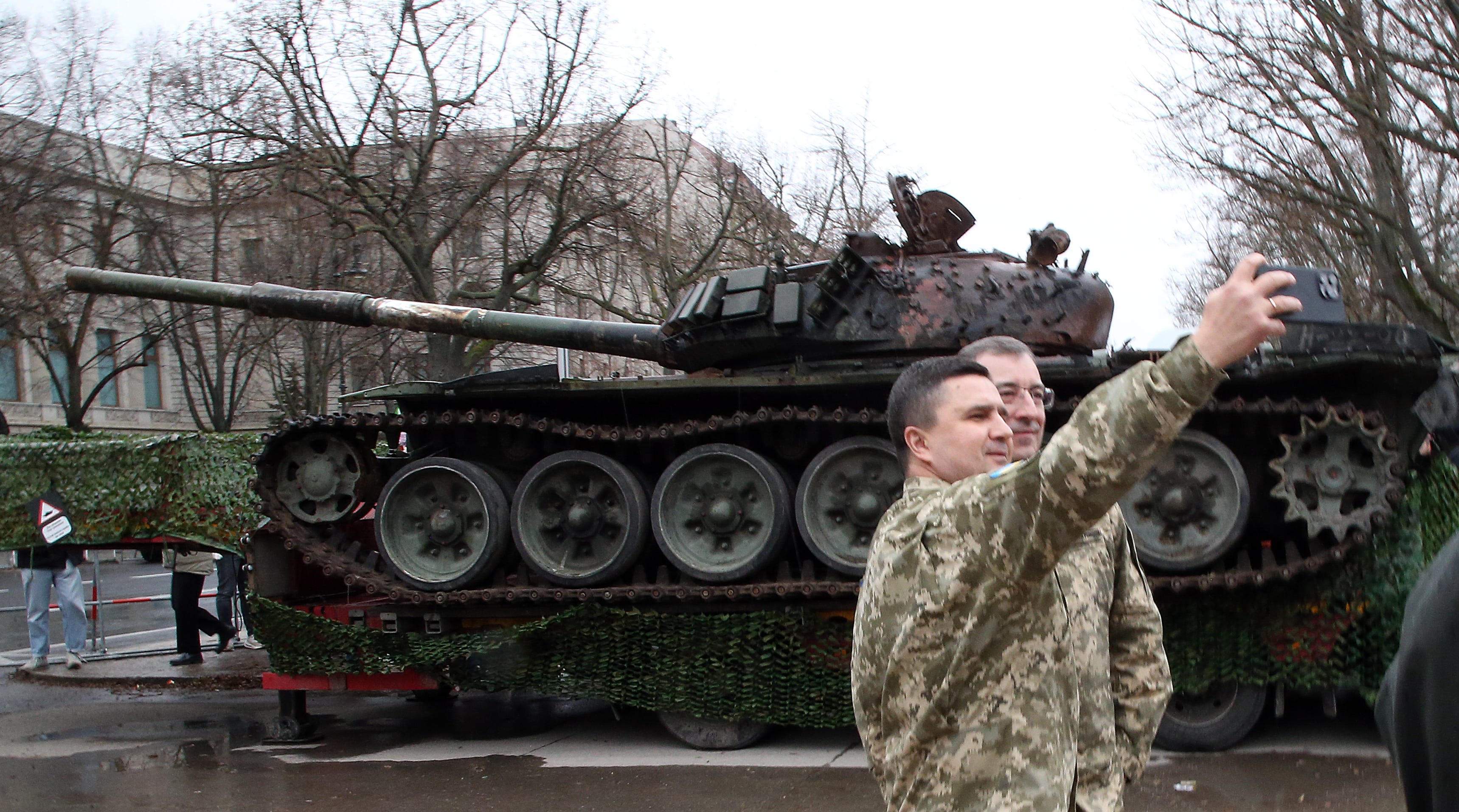 Ukrainische Soldaten stehen auf der Straße Unter den Linden vor einem von der ukrainischen Armee abgeschossenen russischen T-72-Panzer und machen ein Selfie.  Der Panzer wurde wegen des Jahrestages des Ukrainekriegs vor der russischen Botschaft (l) in unmittelbarer Nähe des Brandenburger Tors aufgestellt.
