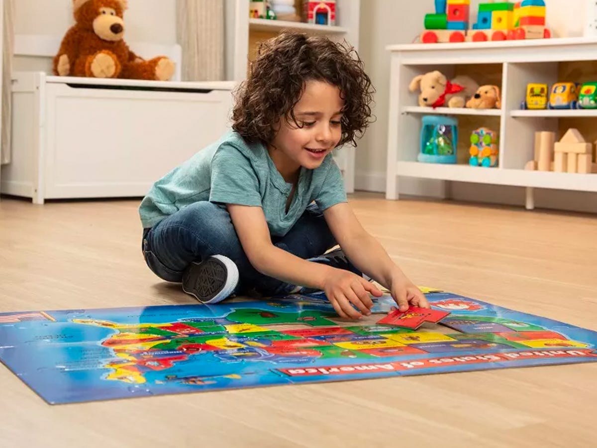 Kind, das das Melissa und Doug USA Map Bodenpuzzle zusammensetzt, während es auf einem Holzboden in einem Spielzimmer sitzt.