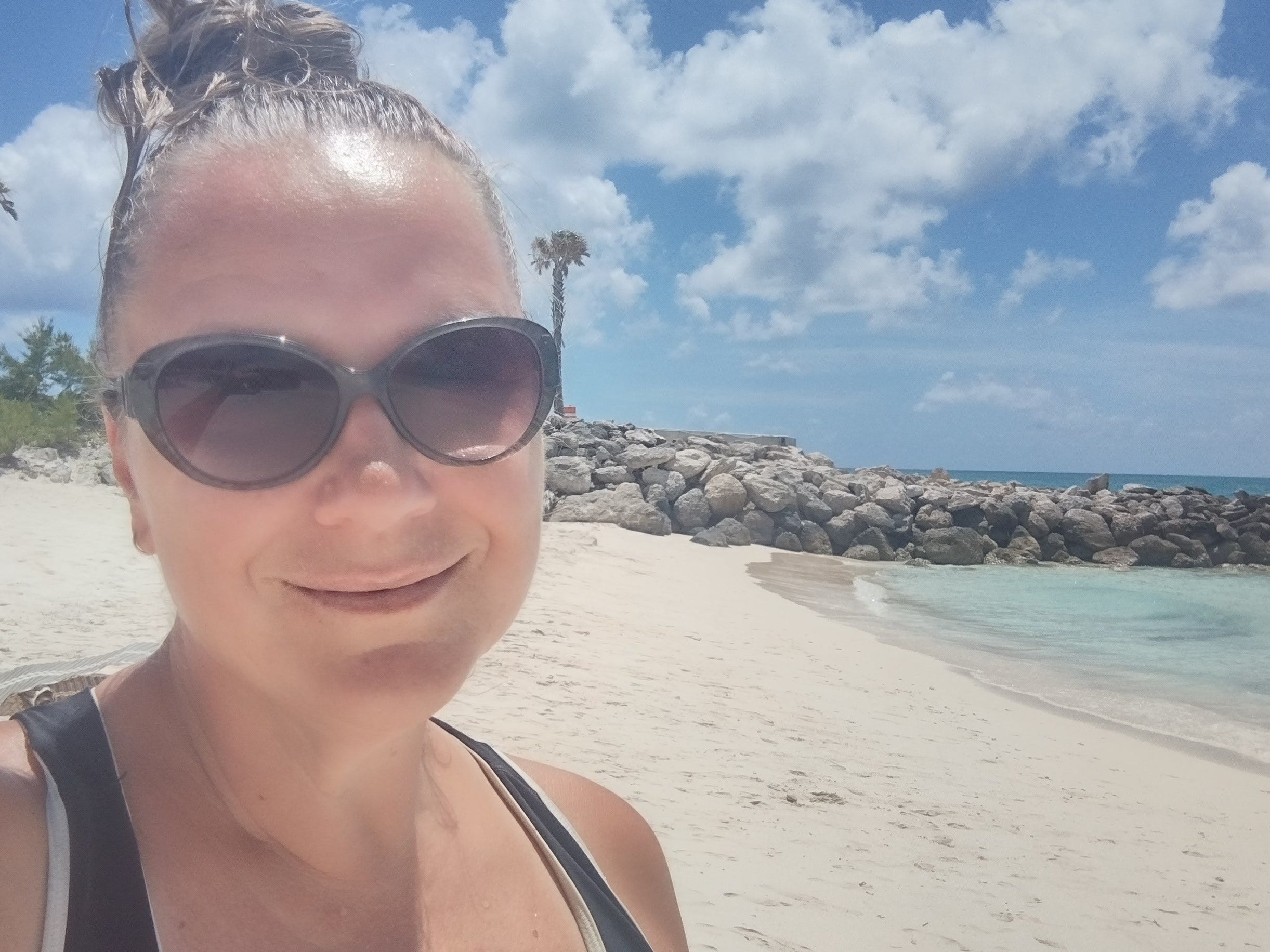 Frau mit schwarzer Sonnenbrille lächelt für ein Selfie am Strand