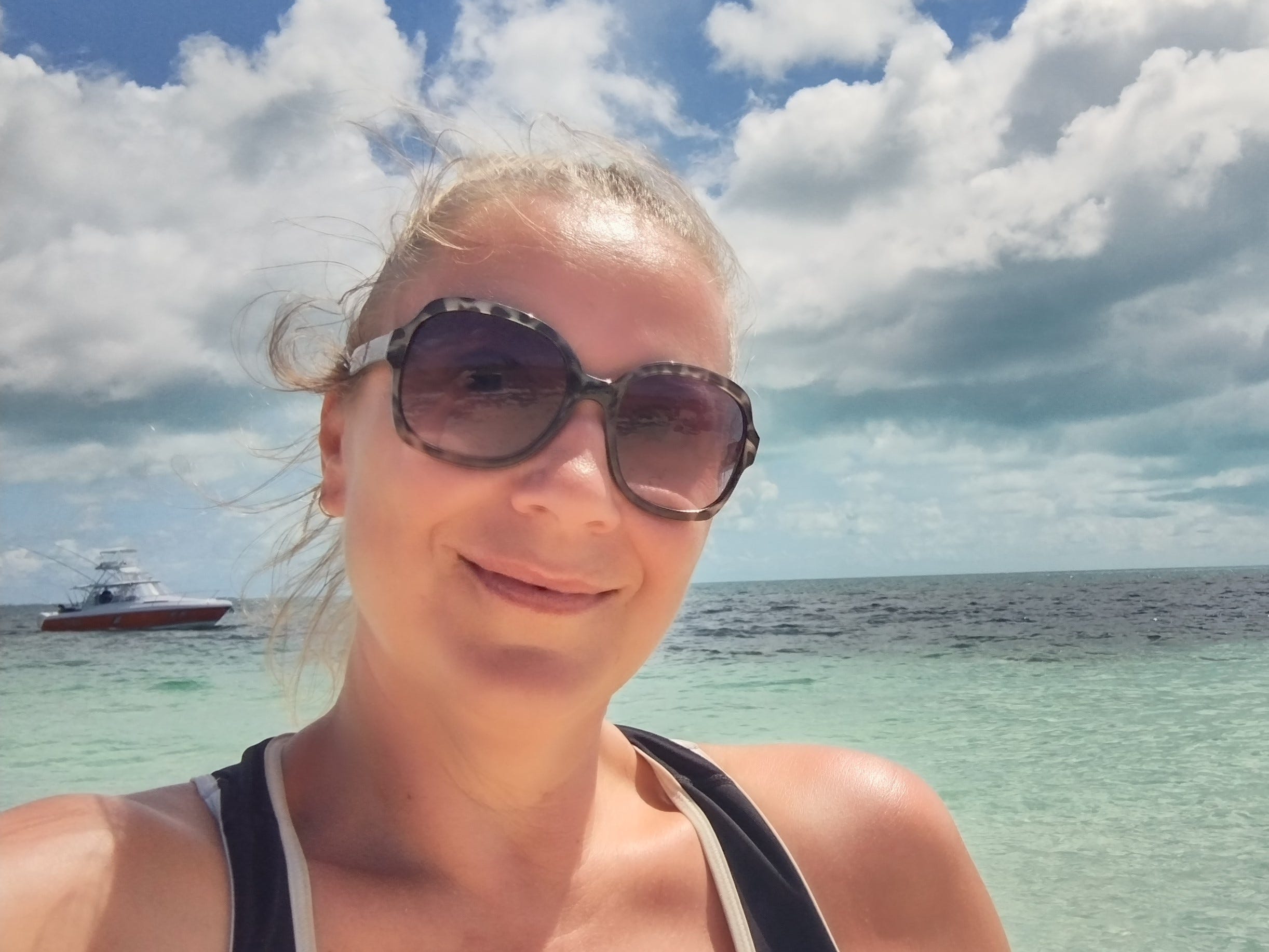 Frau mit dunkler Sonnenbrille lächelt für ein Selfie vor dem Meer