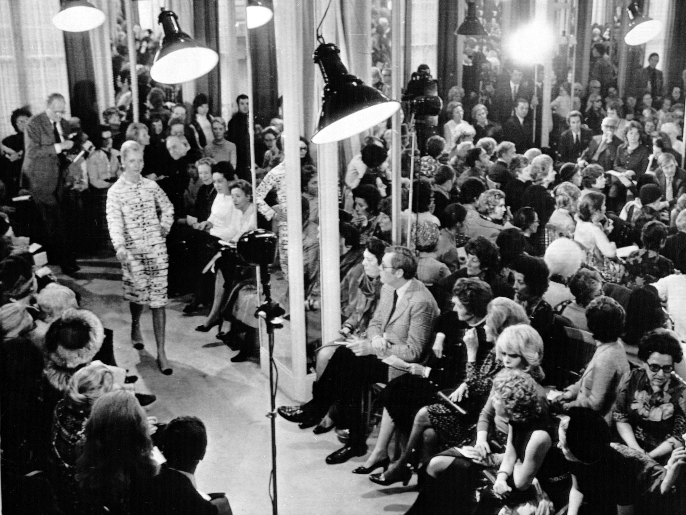 Menschen sitzen in einem überfüllten Raum und sehen zu, wie Models mit Chanel den Laufsteg hinunterlaufen