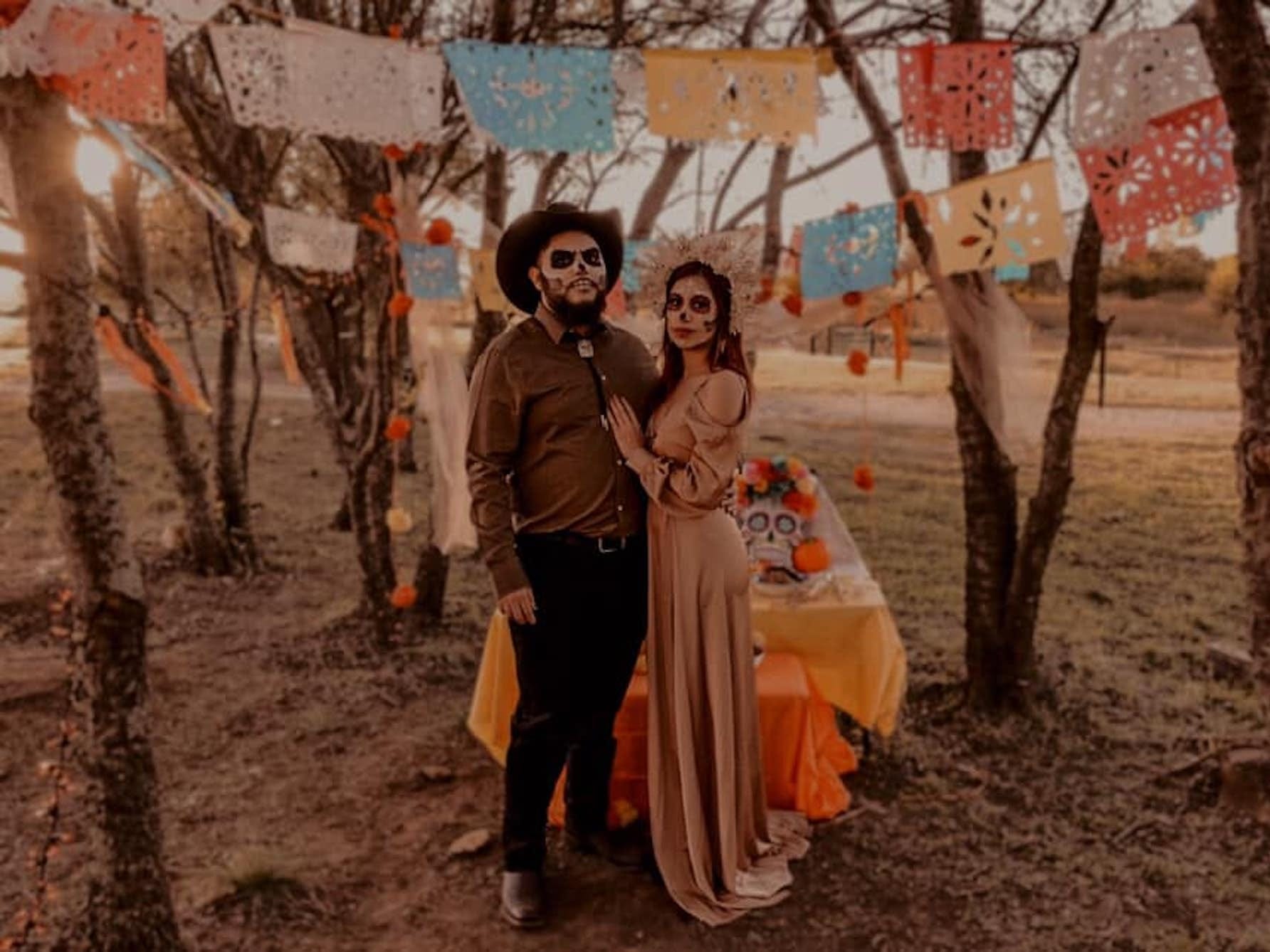 Ein Paar steht in traditioneller Kleidung für Día de Muertos auf einem Feld.