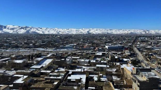 Blick auf eine kleine afghanische Stadt, schneebedeckte Berge in der Ferne und einen blauen Himmel