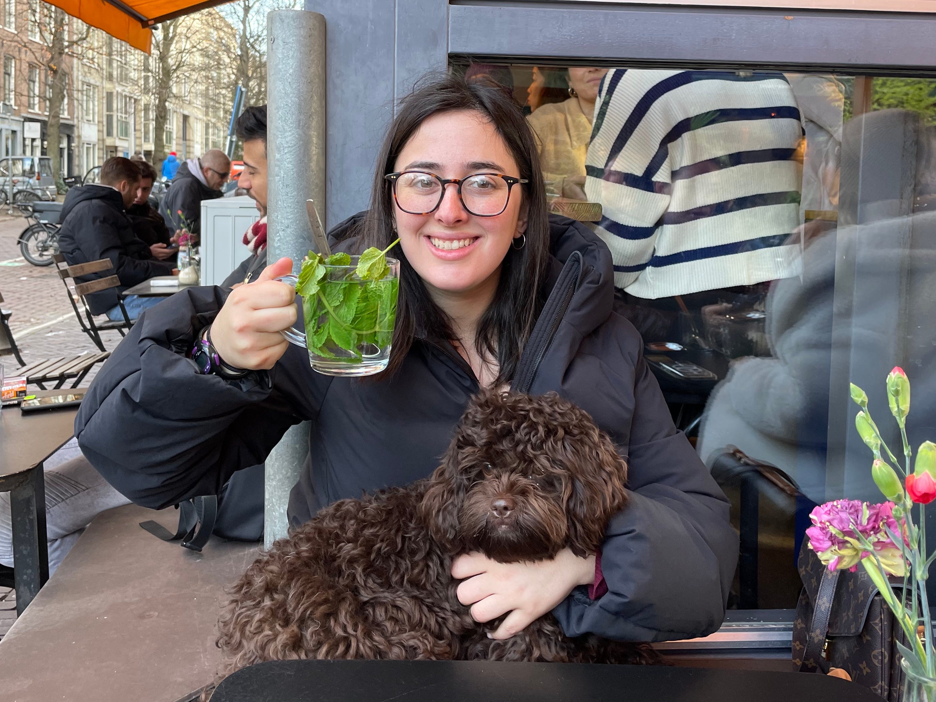 hannah hält eine klasse grünen tee mit einem hund auf ihrem schoß in einem restaurant in europa