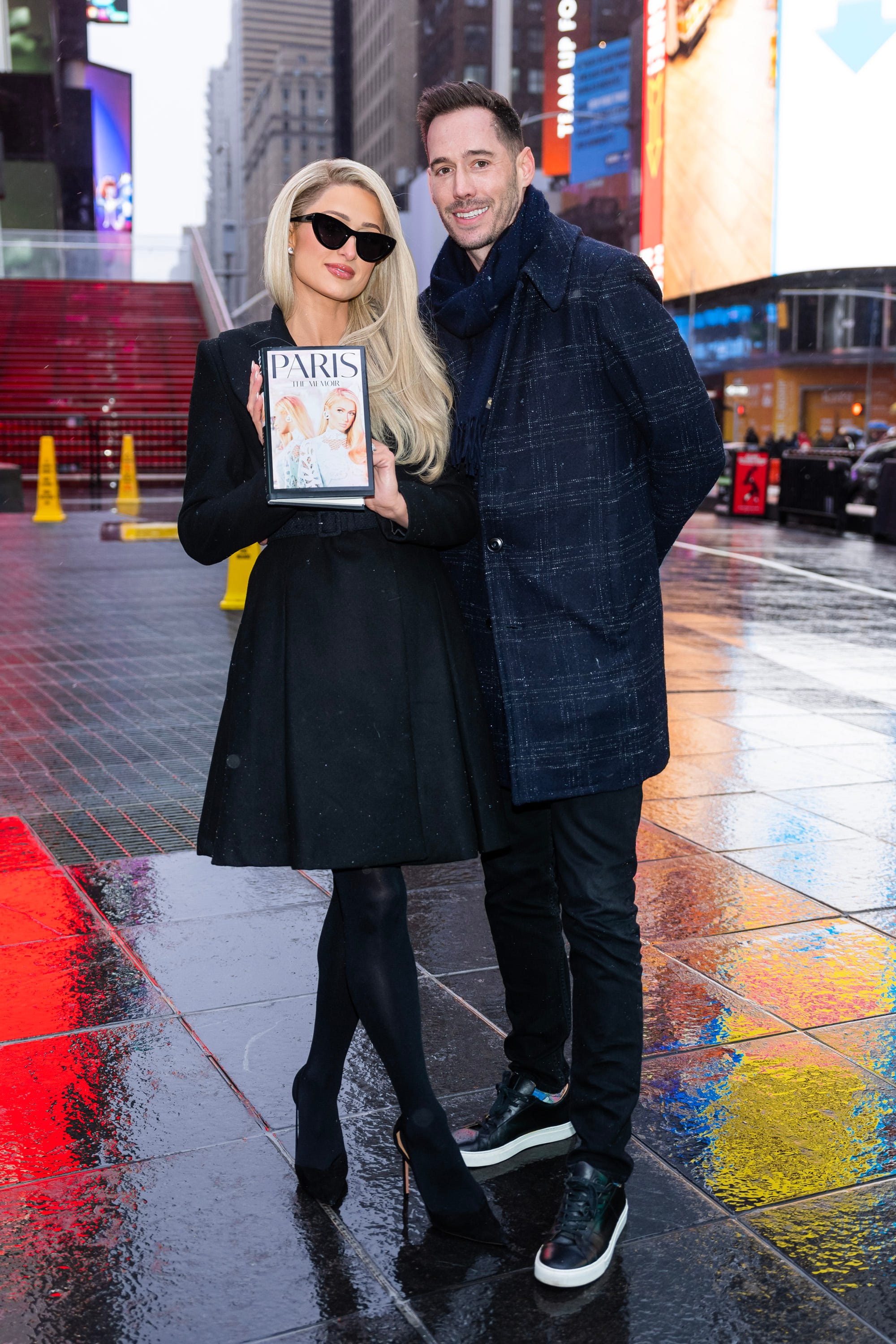 Paris Hilton hält ihre neuen Memoiren neben ihrem Ehemann Carter Reum auf dem Times Square in New York City.