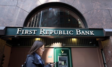 Eine Frau, die auf ihre Phomne blickt, geht an der grün-goldenen Fassade einer Filiale der First Republic Bank vorbei