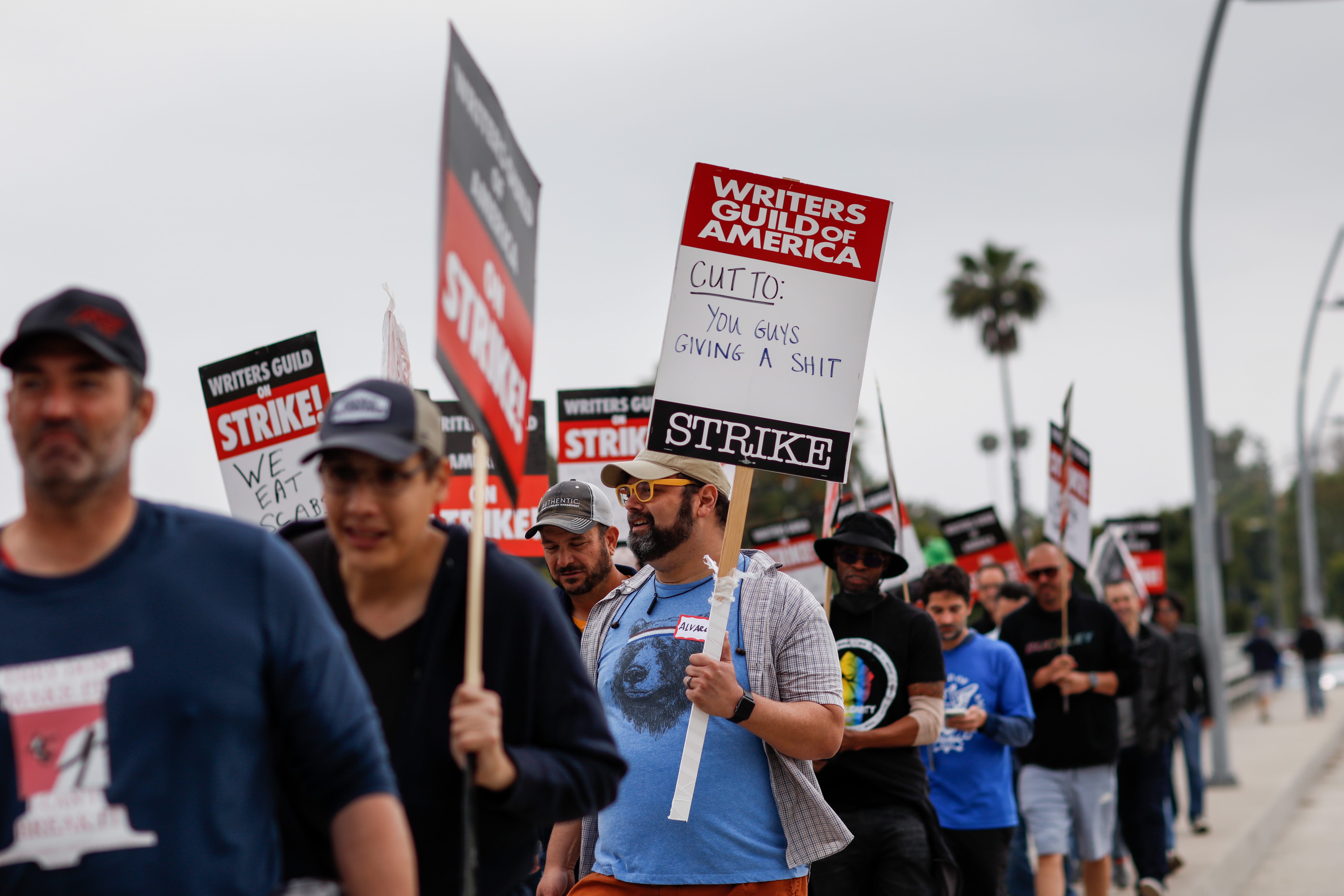 Ein Unterstützer des Streiks der Writers Guild of America geht mit einem Schild mit der Aufschrift „Schnitt an: Euch ist es scheißegal“ spazieren, während Menschen am Dienstag, den 9. Mai, entlang der Colfax Avenue im Radford Studios Center in Studio City, Kalifornien, demonstrieren. 2023.
