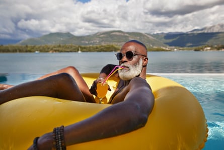 Mann trinkt Saft in aufblasbarem Ring. Glatzköpfiger älterer Mann mit Sonnenbrille, während er im Urlaub Saft in aufblasbarem Ring trinkt