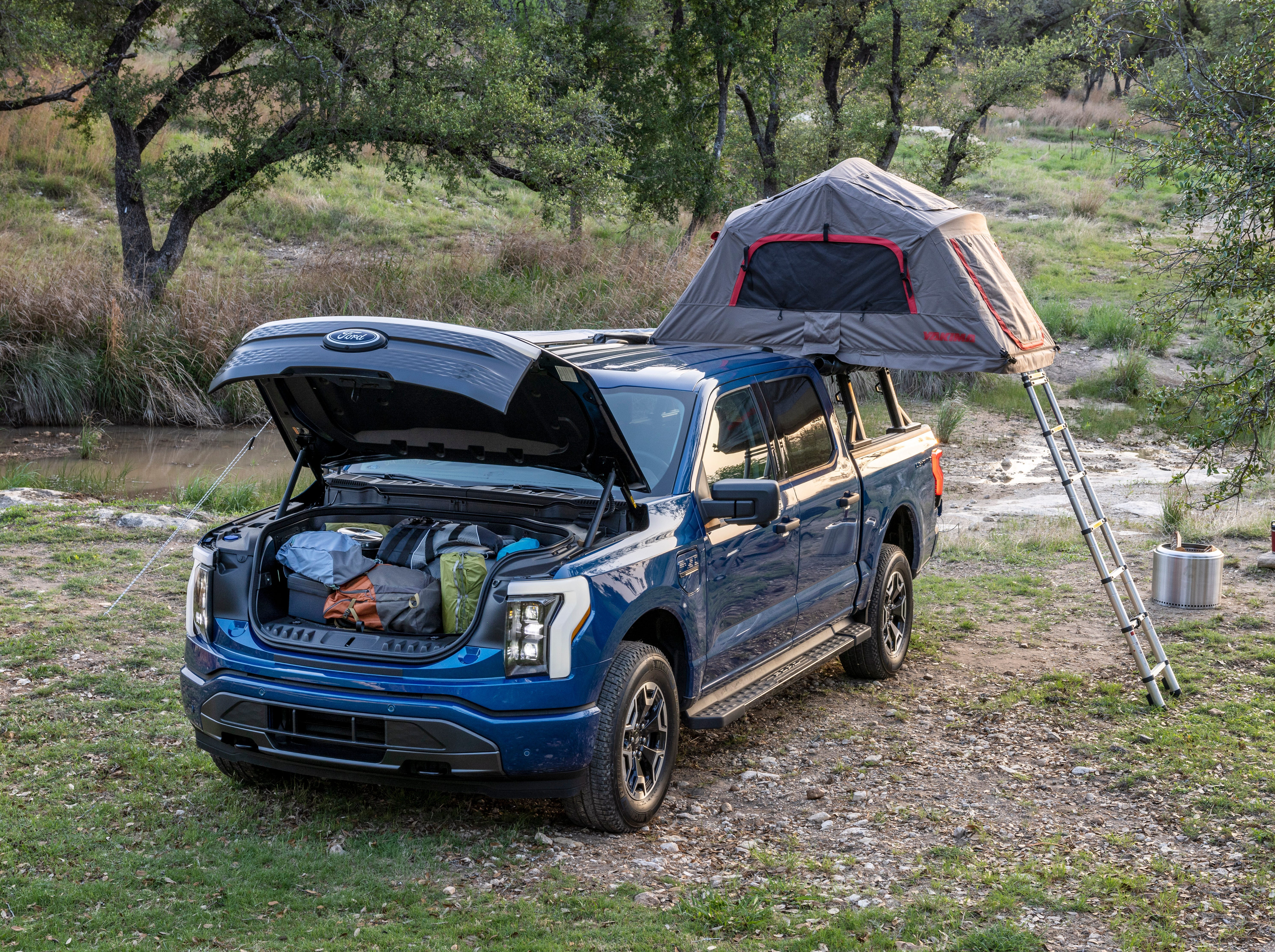 Ein blauer Lastwagen voller Campingausrüstung und einem Zelt mitten in einem Waldgebiet.