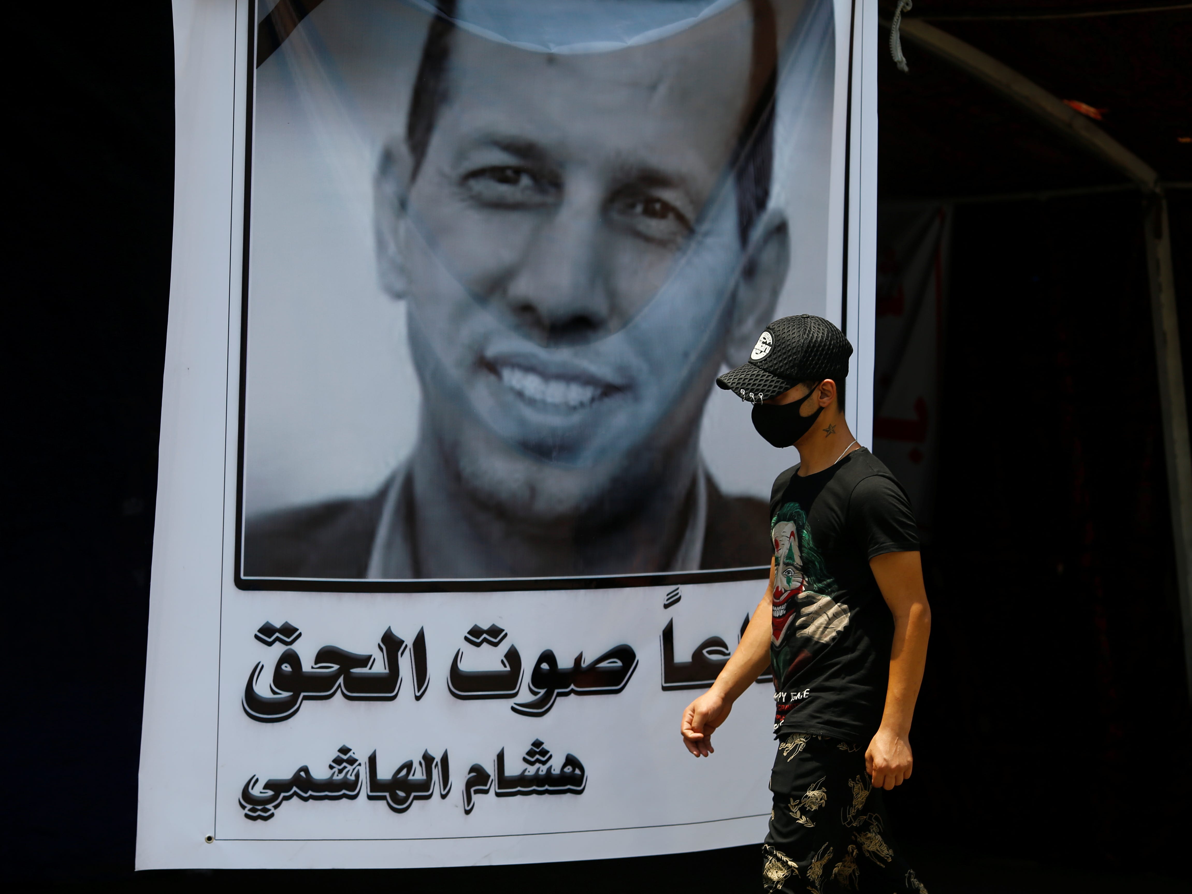 Ein Demonstrant geht an einem Plakat von Hisham al Hashimi vorbei