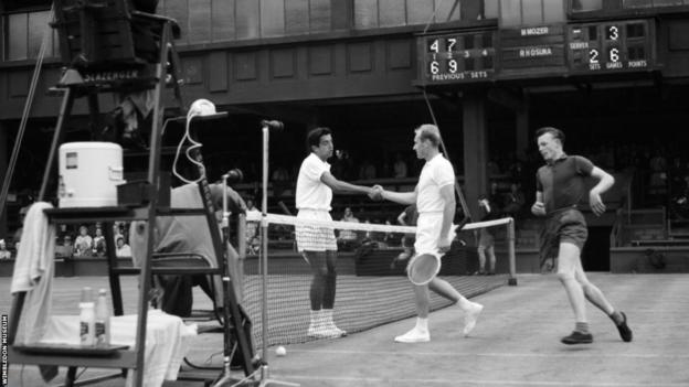Sam Hill rennt um das Netz, während sich Spieler Anfang der 1960er Jahre auf einem Wimbledon-Turnierplatz die Hand schütteln