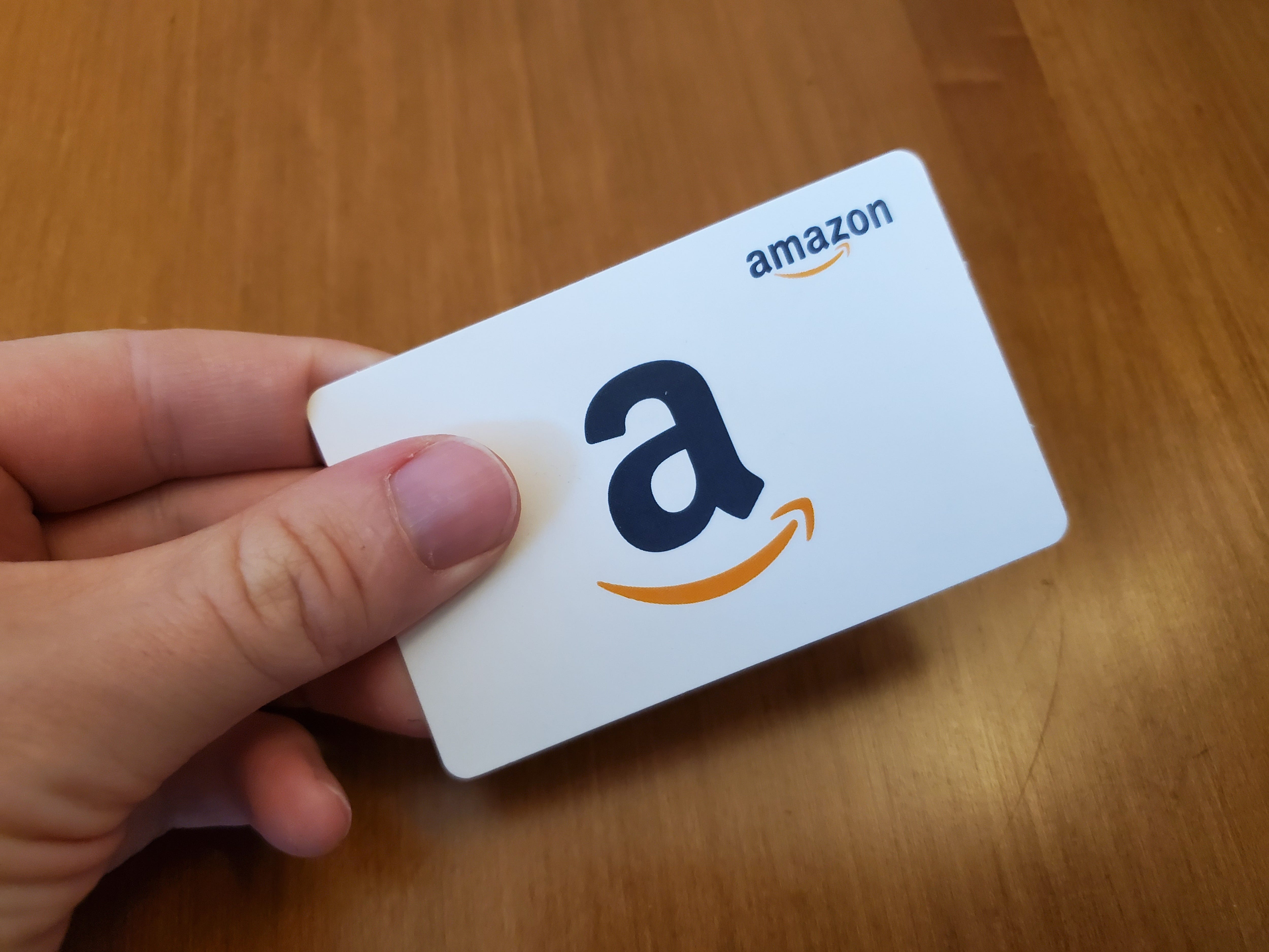 Die Hand einer Person hält eine weiße Amazon-Geschenkkarte.